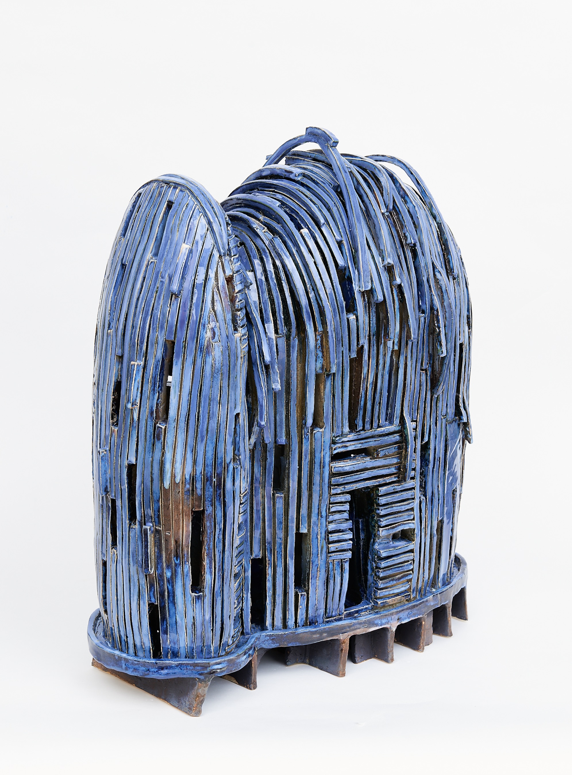 Lydia C. Thompson, Midnight Dreams: Releasing the Shackles, 2023. Ceramics.  22 x 8 x 24". A blue rounded dwelling made with lifting clay strips made primarily with light blue with some brown popping out. It's resting on a light brown pallet.