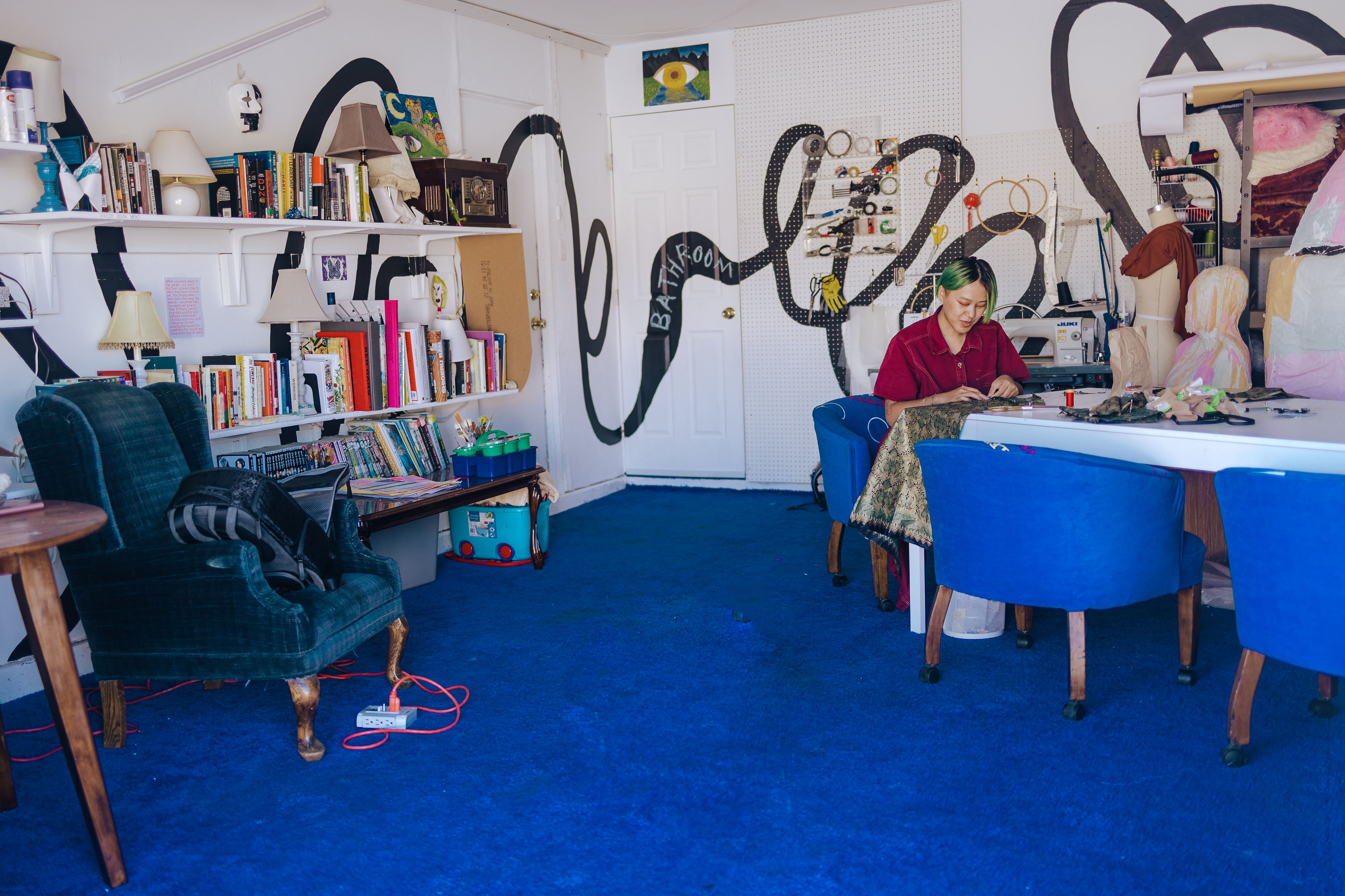 Photo taken by Mario Ramirez of an expanded view of the Cloud House, where you see a wider view of the library, the different sitting areas and table that are for use. On the walls there is a black extended squiggly line that wraps all around the space.