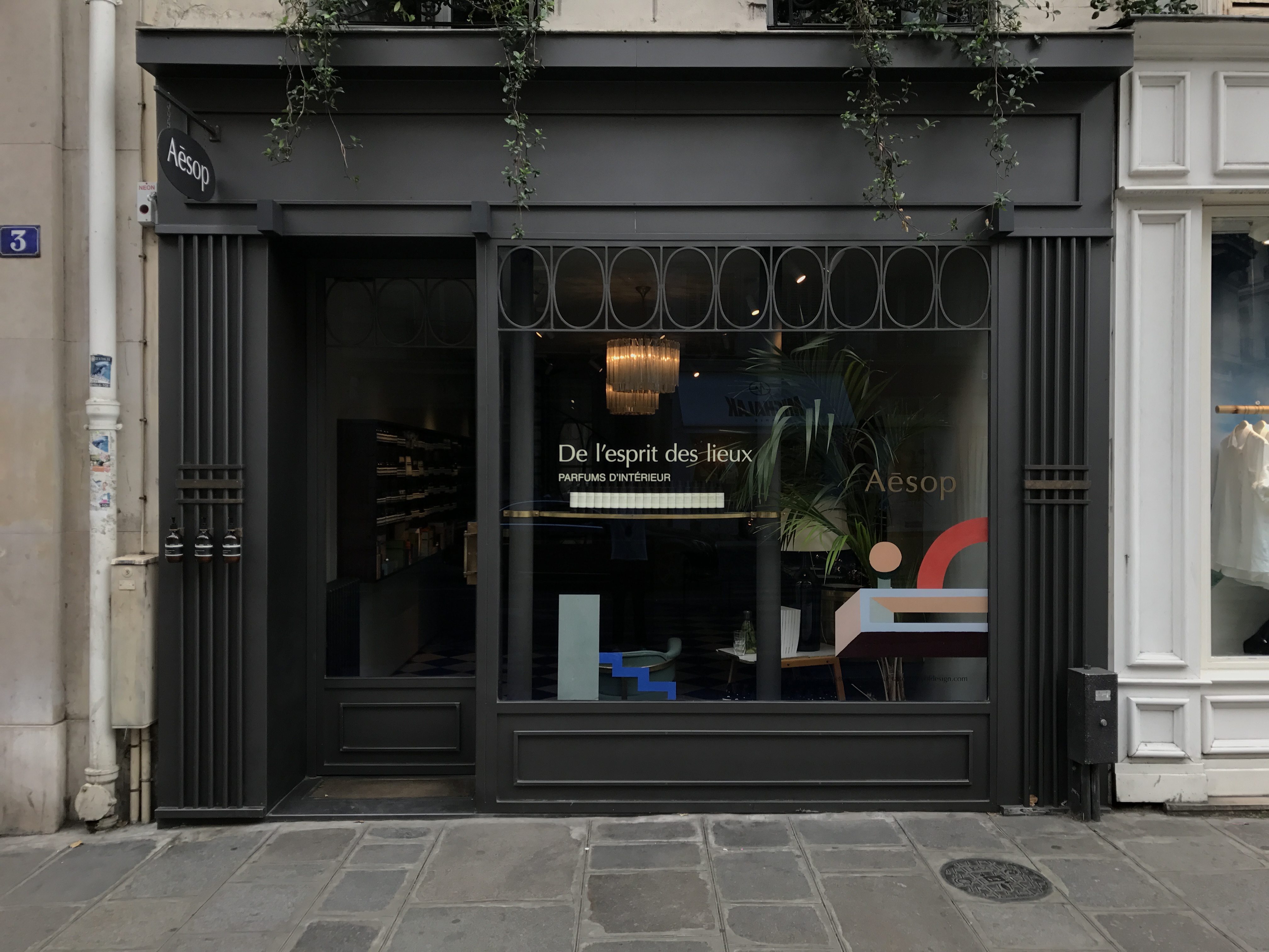 A streetscape featuring the window display of a Parisian signature store. The vinyl reads: de l'esprit des lieux.