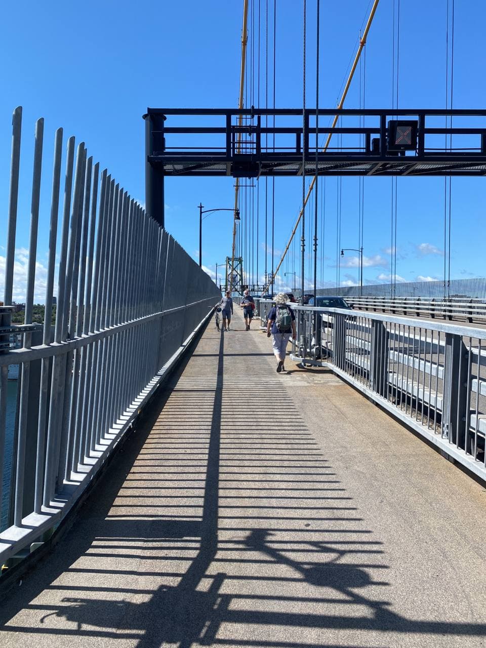 People walking across the Macdonald Bridge, wires on the right side and a fence on the left side