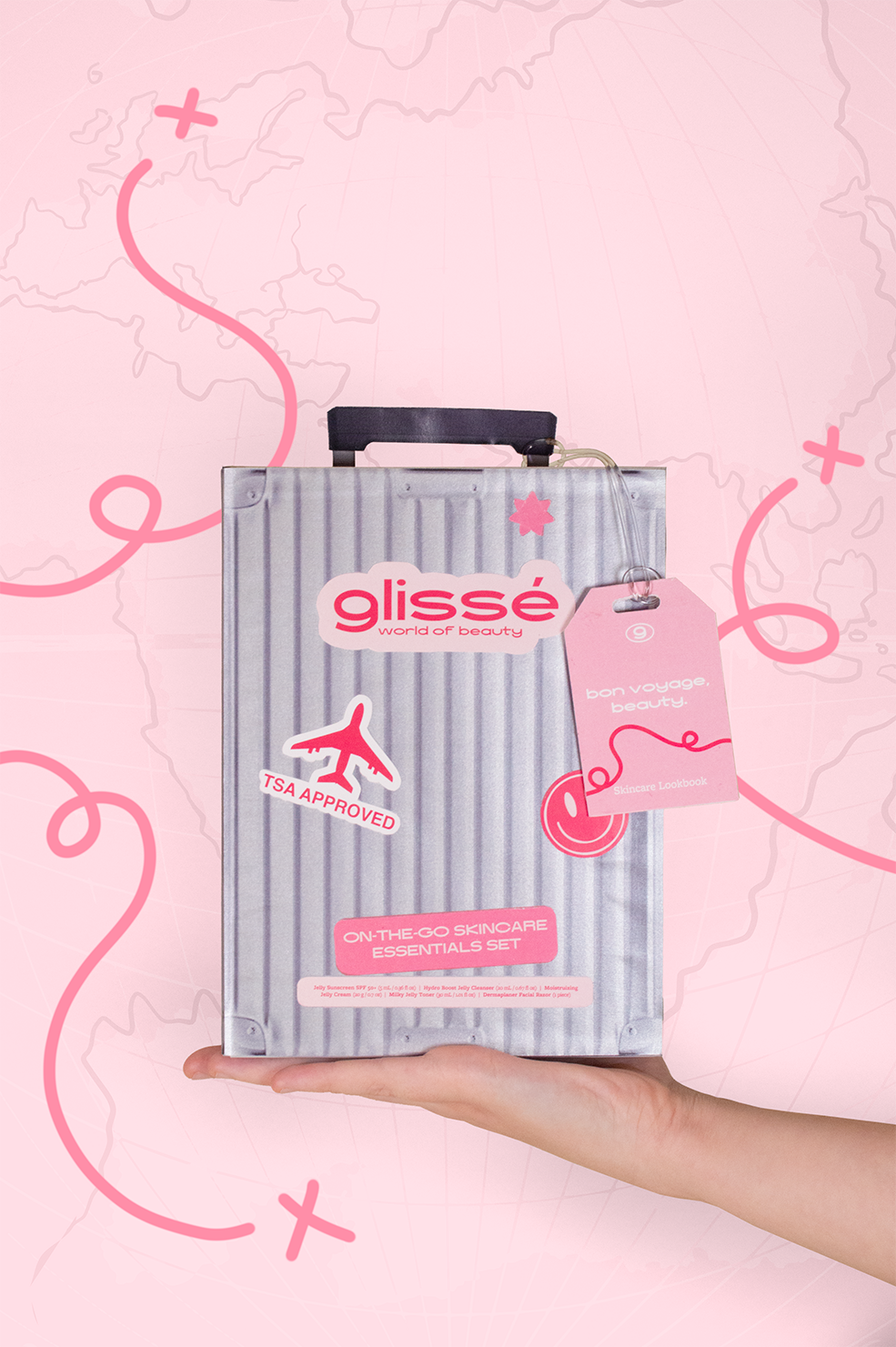 Pink studio shot featuring a hand holding out a metallic suitcase package box titled "Glisse World of Beauty." The background features a map and meandering lines pattern to further enhance the traveling aspect of this product.