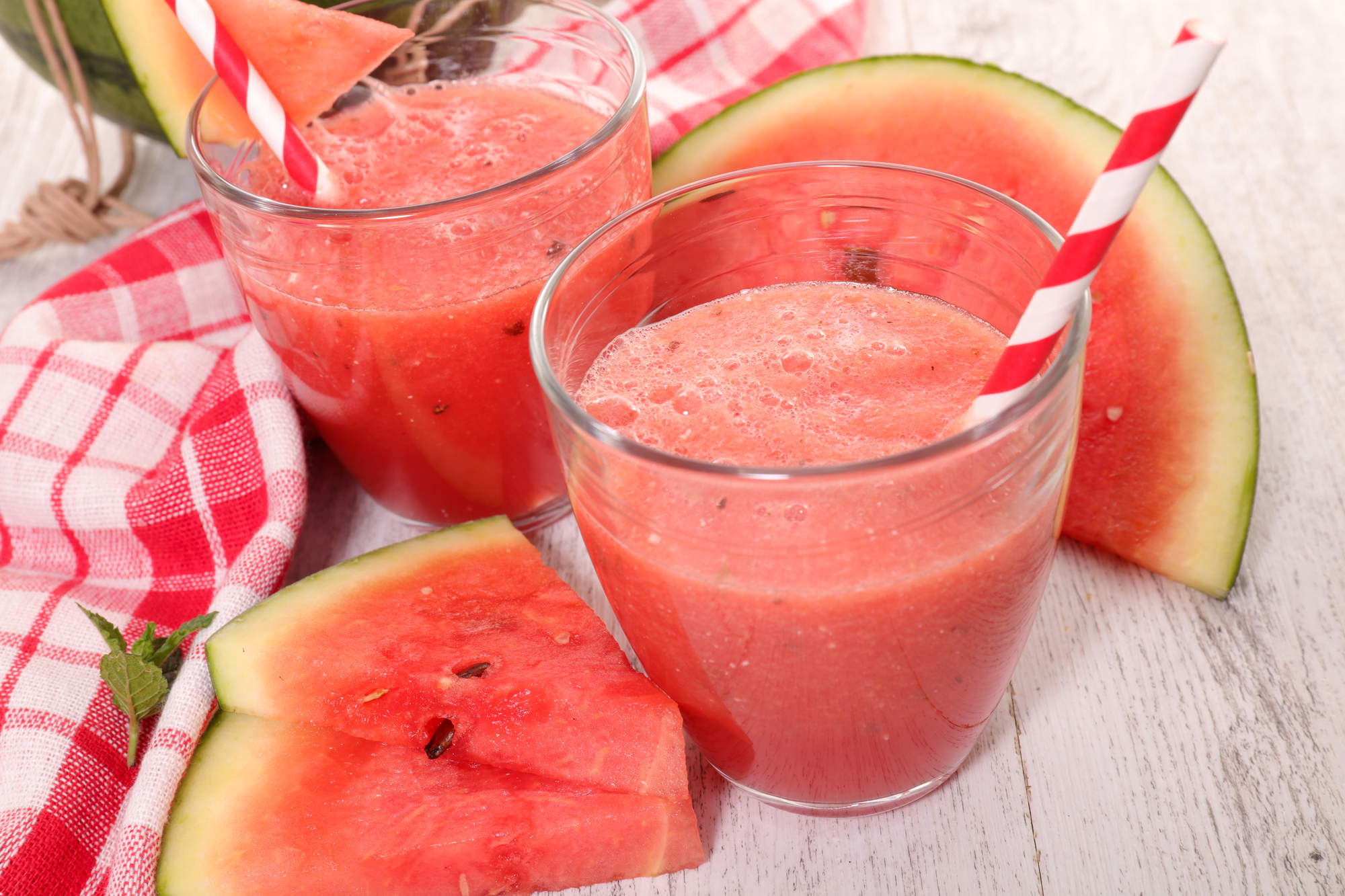 An up-close view of an artfully staged picture of watermelon smoothie and cut pieces of watermelon on wood table