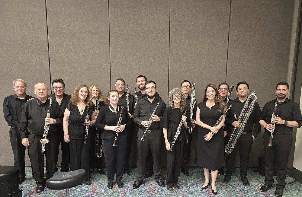 A group of musicians standing in a room, each holding their instrument, and facing the camera.