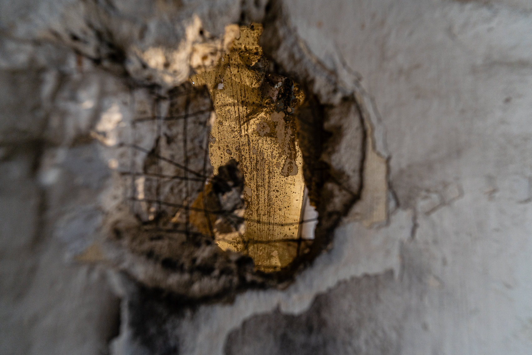 Bild 2 zu Fungillation:  Durch das Loch einer Wand sind verschiedene Strukturen erkennbar. Das innere des Raumes, der nur durch das Loch sichtbar ist, ist beleuchtet und l&auml;sst verschiedene Strukturen und Schatten des Pilzes erkennen.