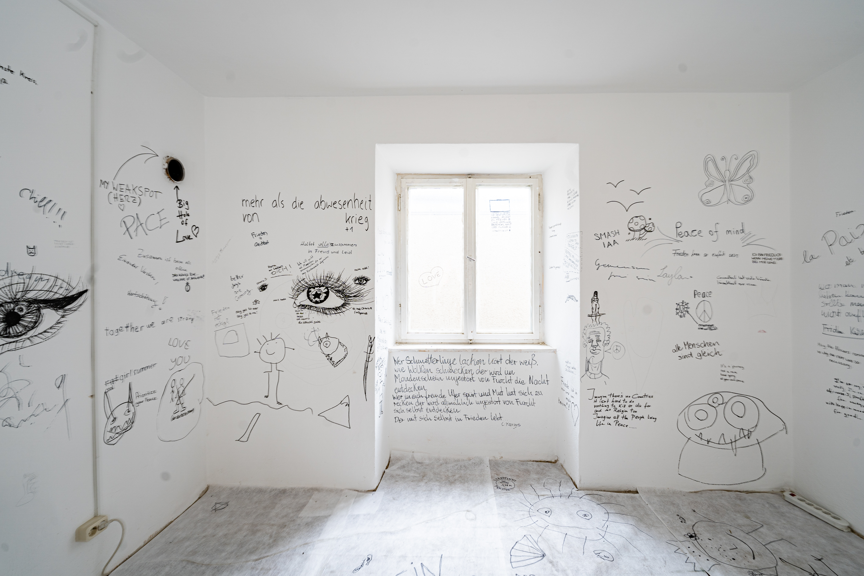 Bild 2 Tischlein deck dich: Eine wei&szlig;e mit schwarz beschriftete Wand und in der Mitte ein Fenster.