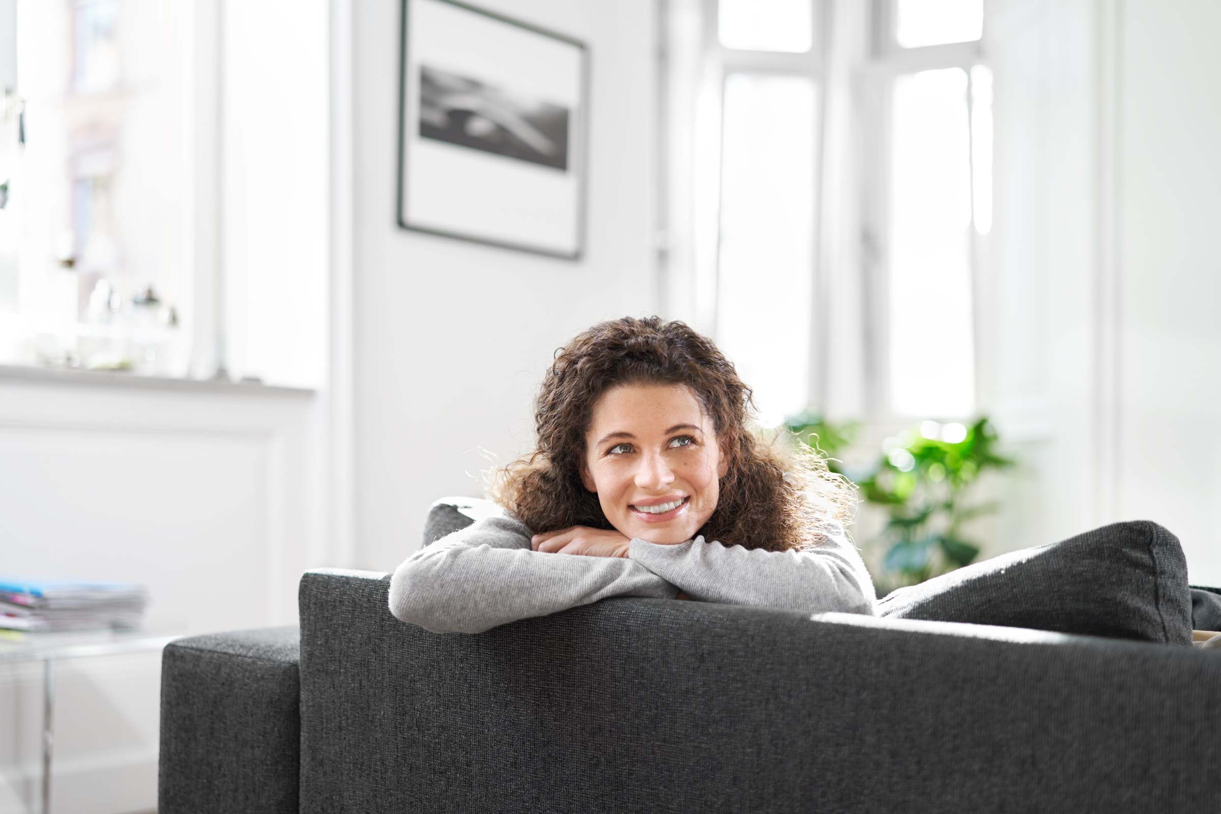 Portrait einer Frau, sitzend auf einer Couch in einem Wohnzimmer.