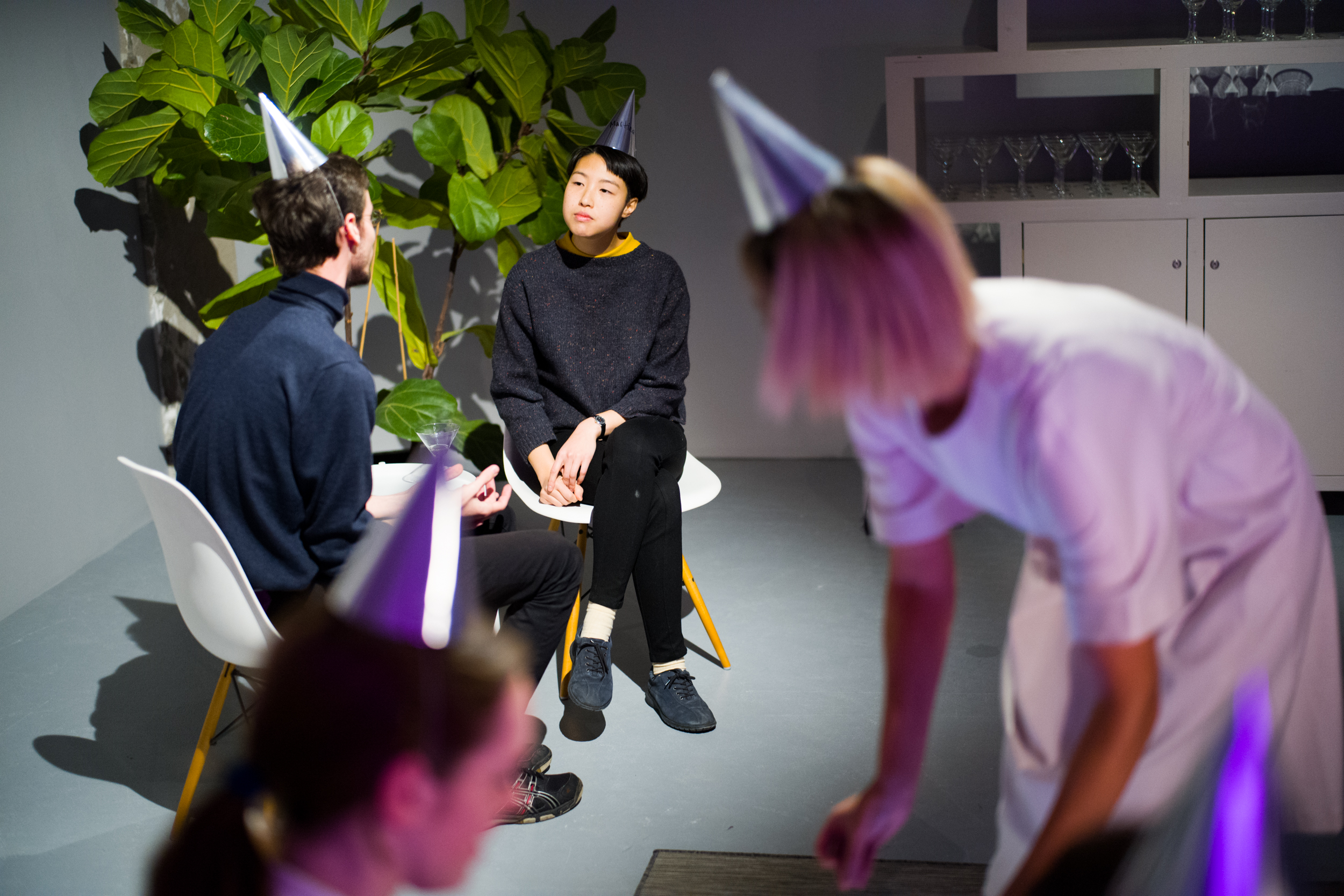 documentation image of two people talking in the background while sitting in individual chairs, and in the blurred foreground lauren hunching down towards someone.