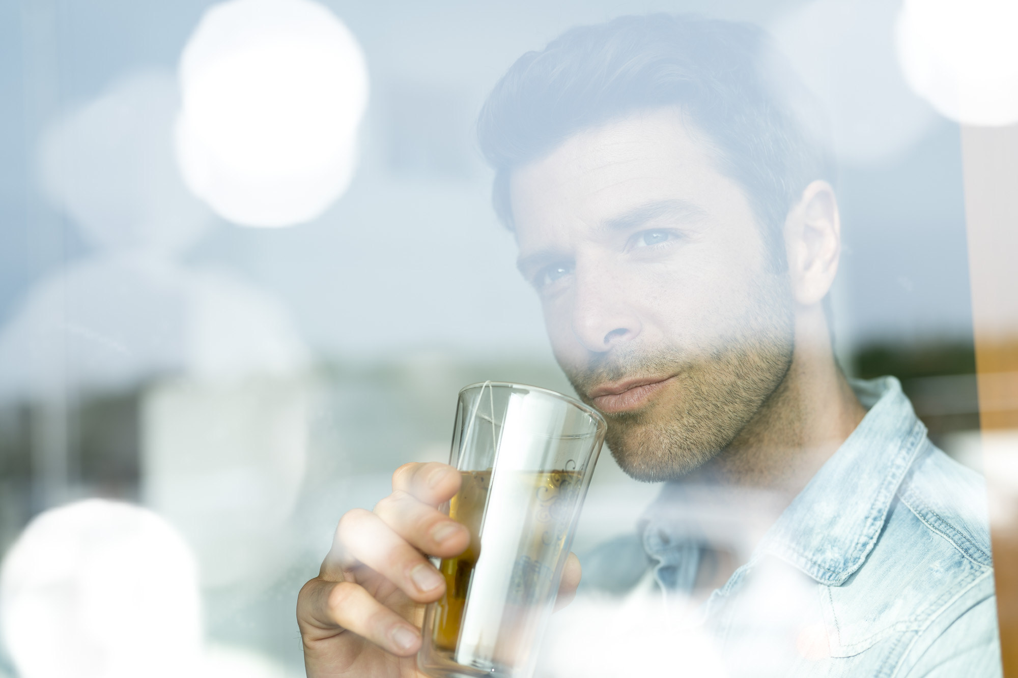 Portrait eines jungen Mannes mit einem Teebecher in der Hand. Portrait durch eine Scheibe mit Bendenflecken.