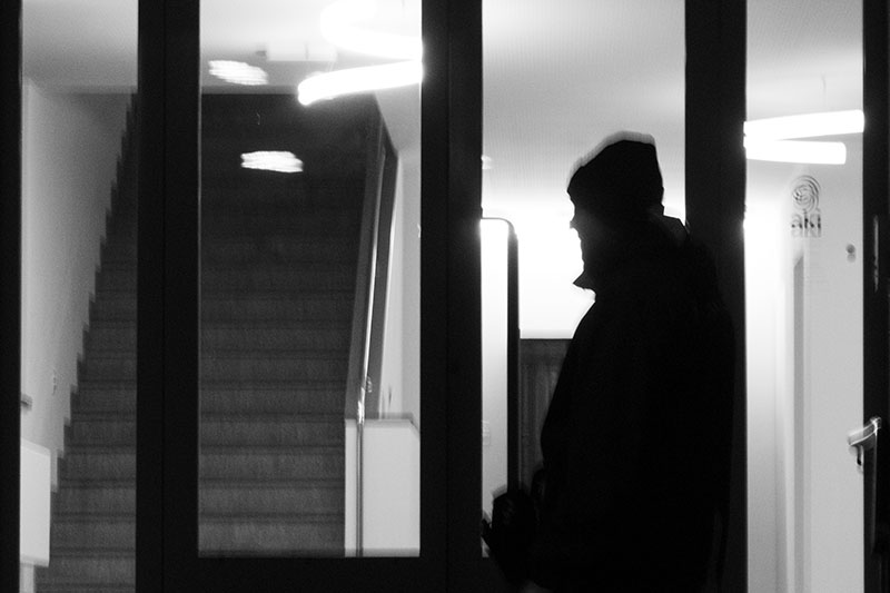 Ein Mann, ganz in schwarz, geht zielstrebig auf das Haus zu und sch&uuml;ttelt den Kopf, als er die offene T&uuml;re sieht.