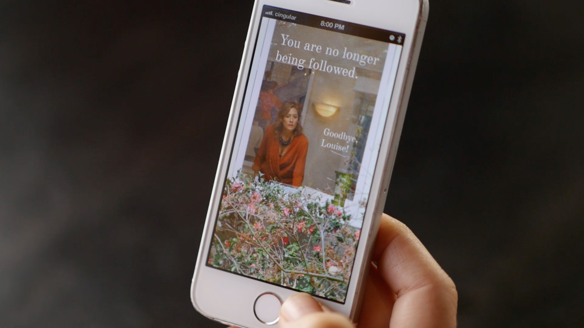 close up image of a hand holding a phone with the screen showing the follower app with "You are no longer being followed" as the header and an image of a person looking out the window as the backgorund.