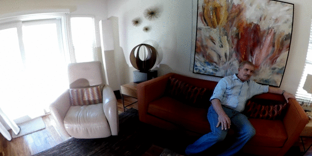 360 video of two people in their living room, one is looking out the window and the other person is sitting on the couch facing the camera.