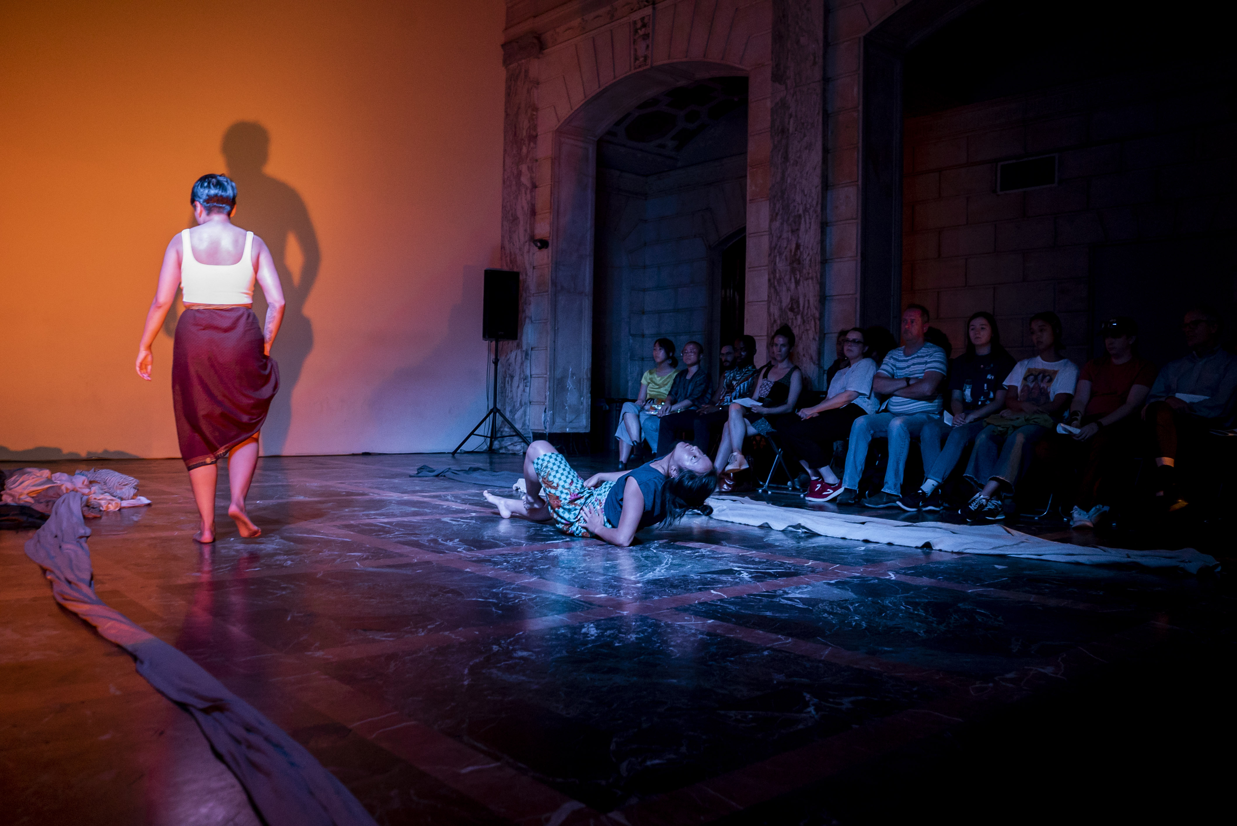 Photo by Cameron Kelly McLeod/ISSUE Project Room: from performance at ISSUE's theater, Annie and Sok's "This Mother/land Fabric:" Sok (L) with back to the camera and Annie (R) on floor, arched back, with audience in the around visible (far R)