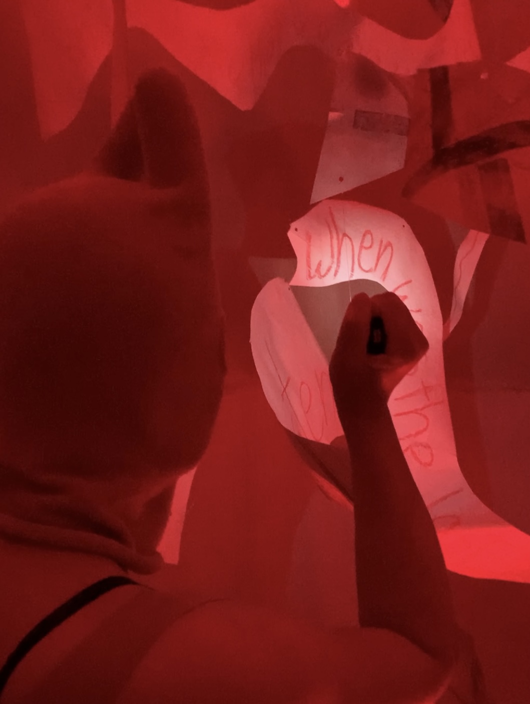 Single close up image shot from behind of a person lighting up the paper sculpture to reveal the words hidden by the red light.