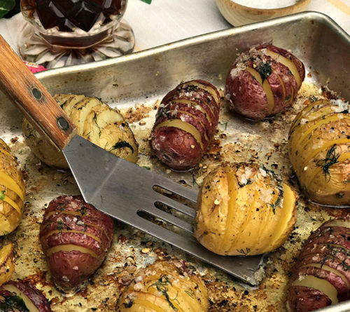 Mini hasselback potatoes cooked on pan with spatula holding one potato