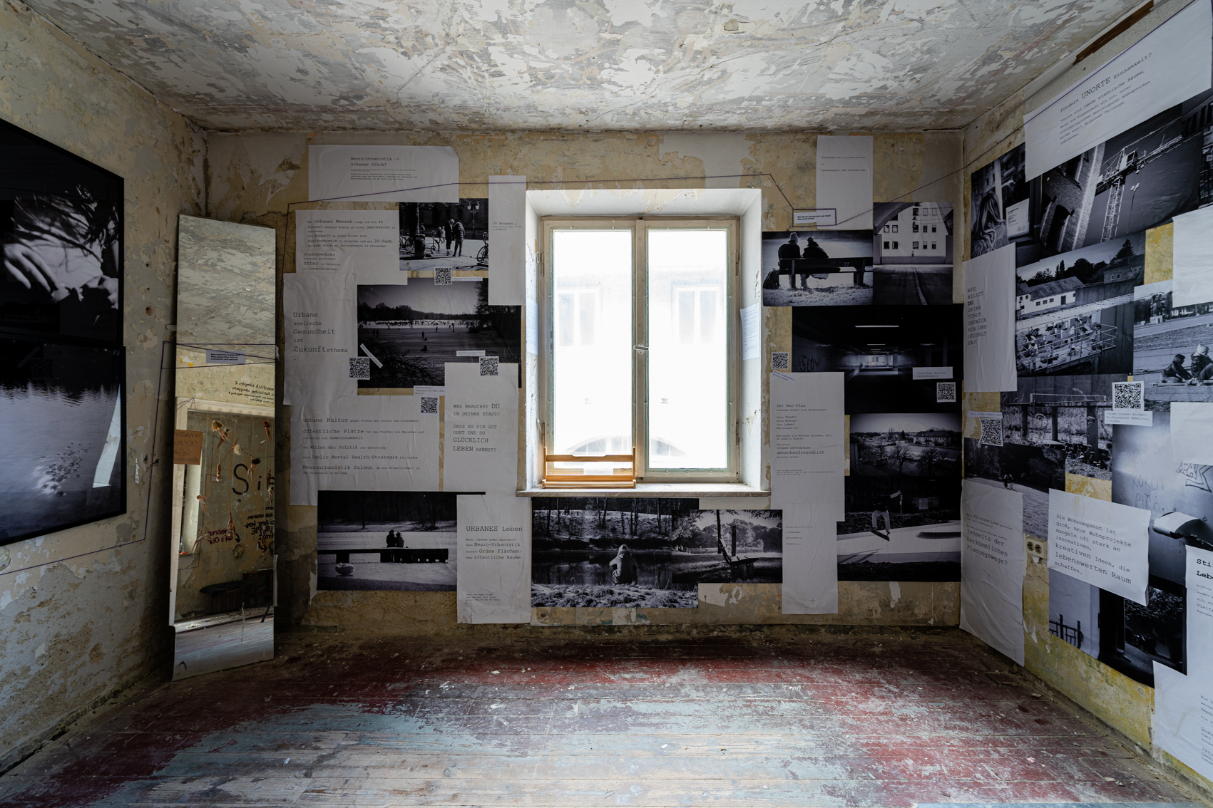 Bild 2 zu Die Bilder der anderen: Das Foto zeigt direkt gegen&uuml;ber des Betrachtenden das einzige Fenster des Raumes. Rechts und links davon weitere Collagen. Im linken Eck steht ein gro&szlig;er l&auml;nglicher Spiegel. 