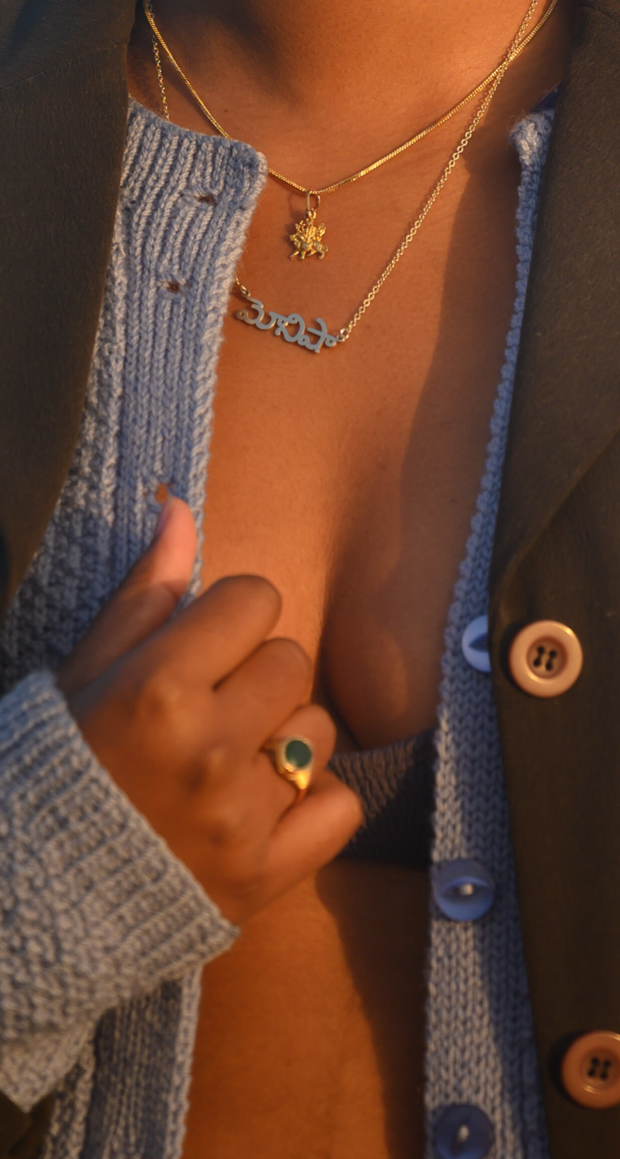 The image is cropped to focus on Monisha’s chest and torso. She wears two gold necklaces, one is of the Hindu goddess Durga.