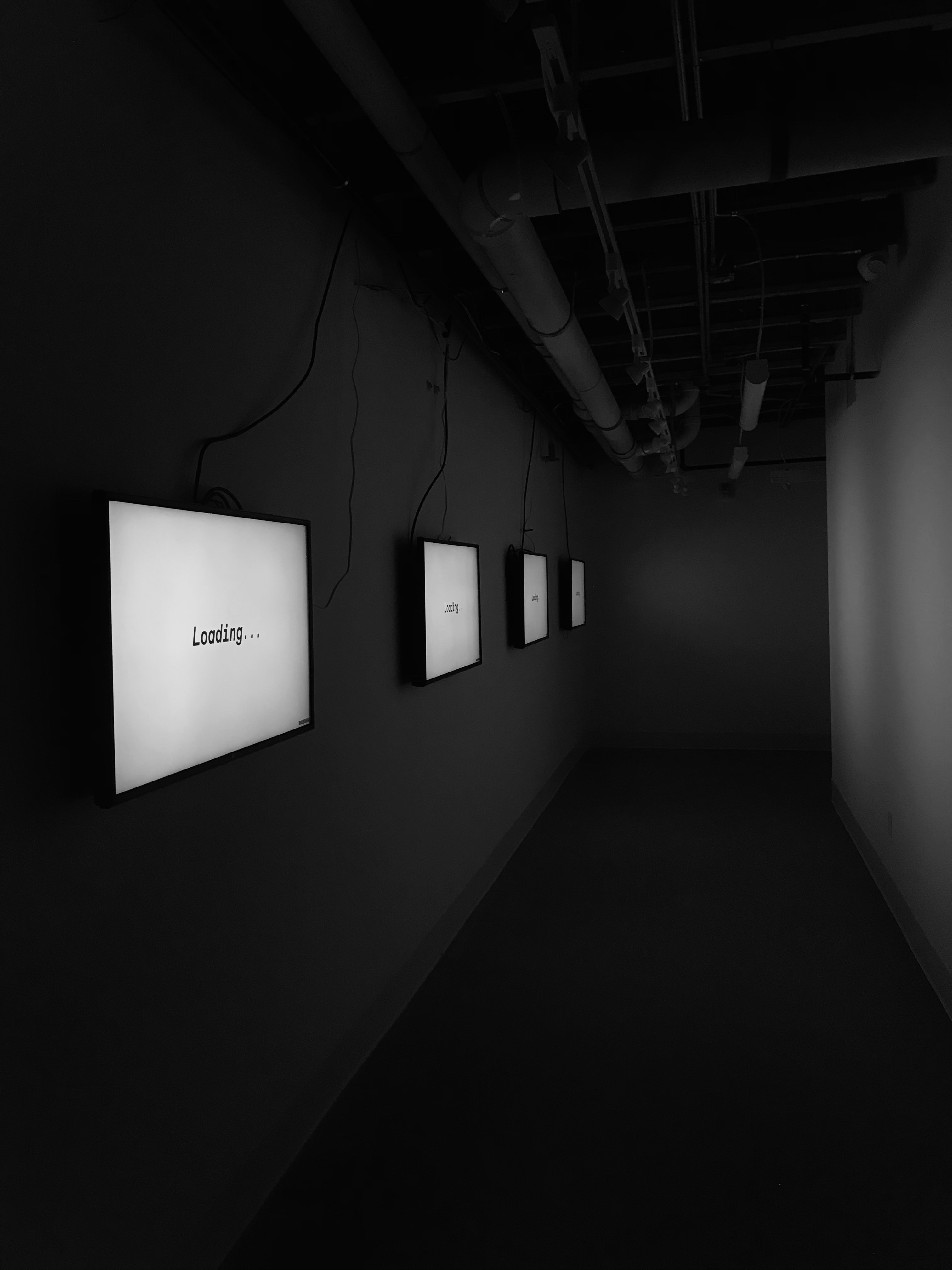 Dark hall of four monitors, white screens with black text loading….