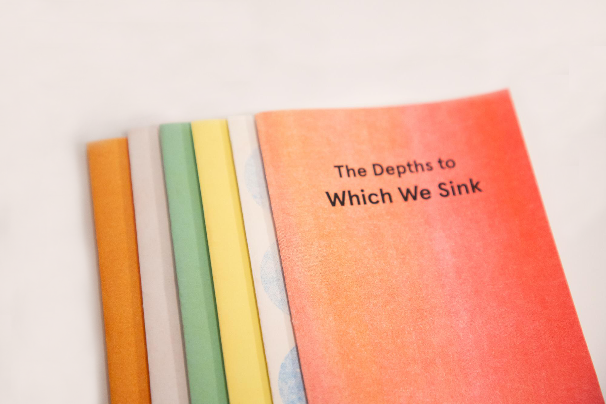 Multiple color variations of a risograph book cover with black text that says, "The Depths to Which We Sink."