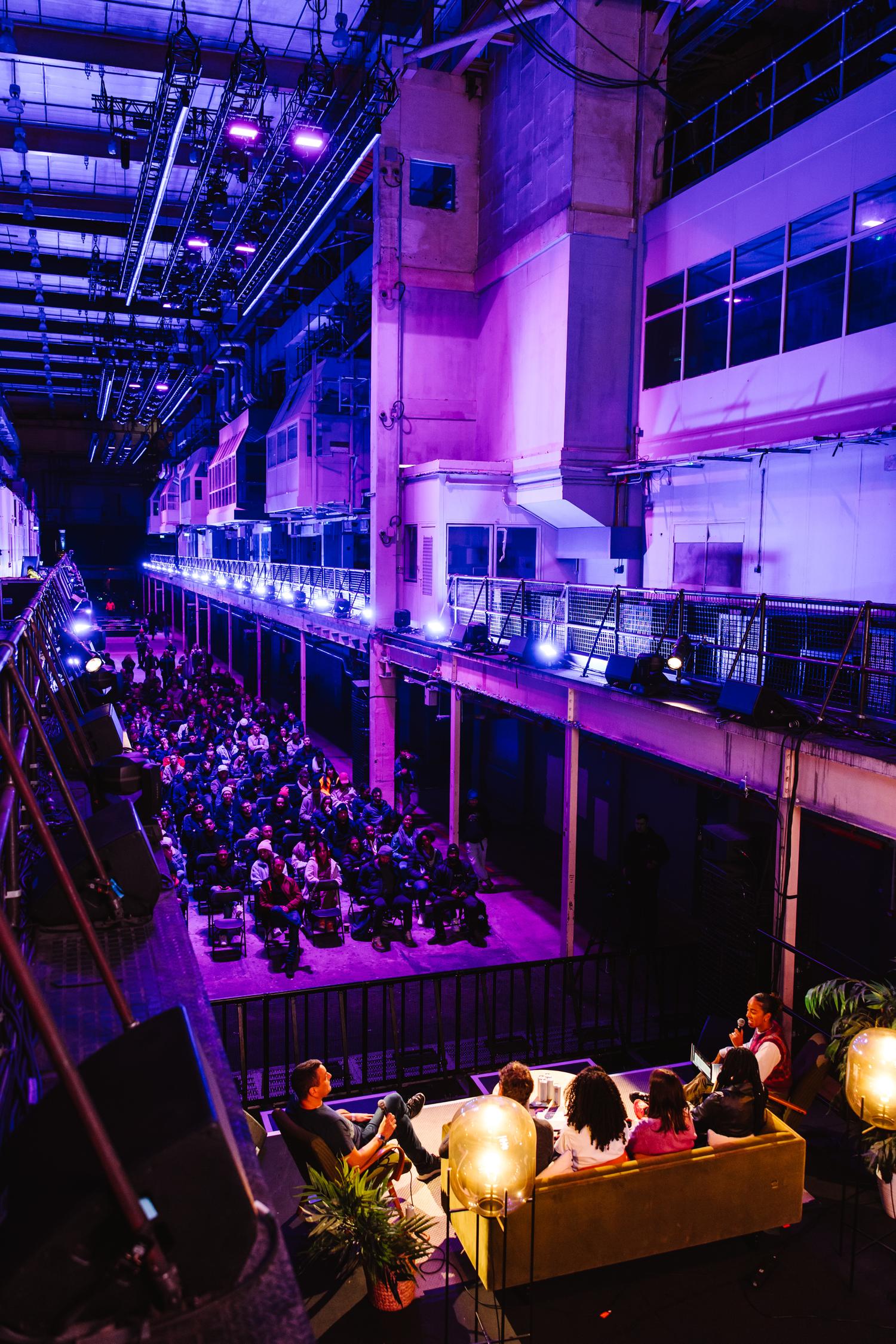 Audience watching panel discussion on stage at AVA London conference in Printworks with purple lighting.
