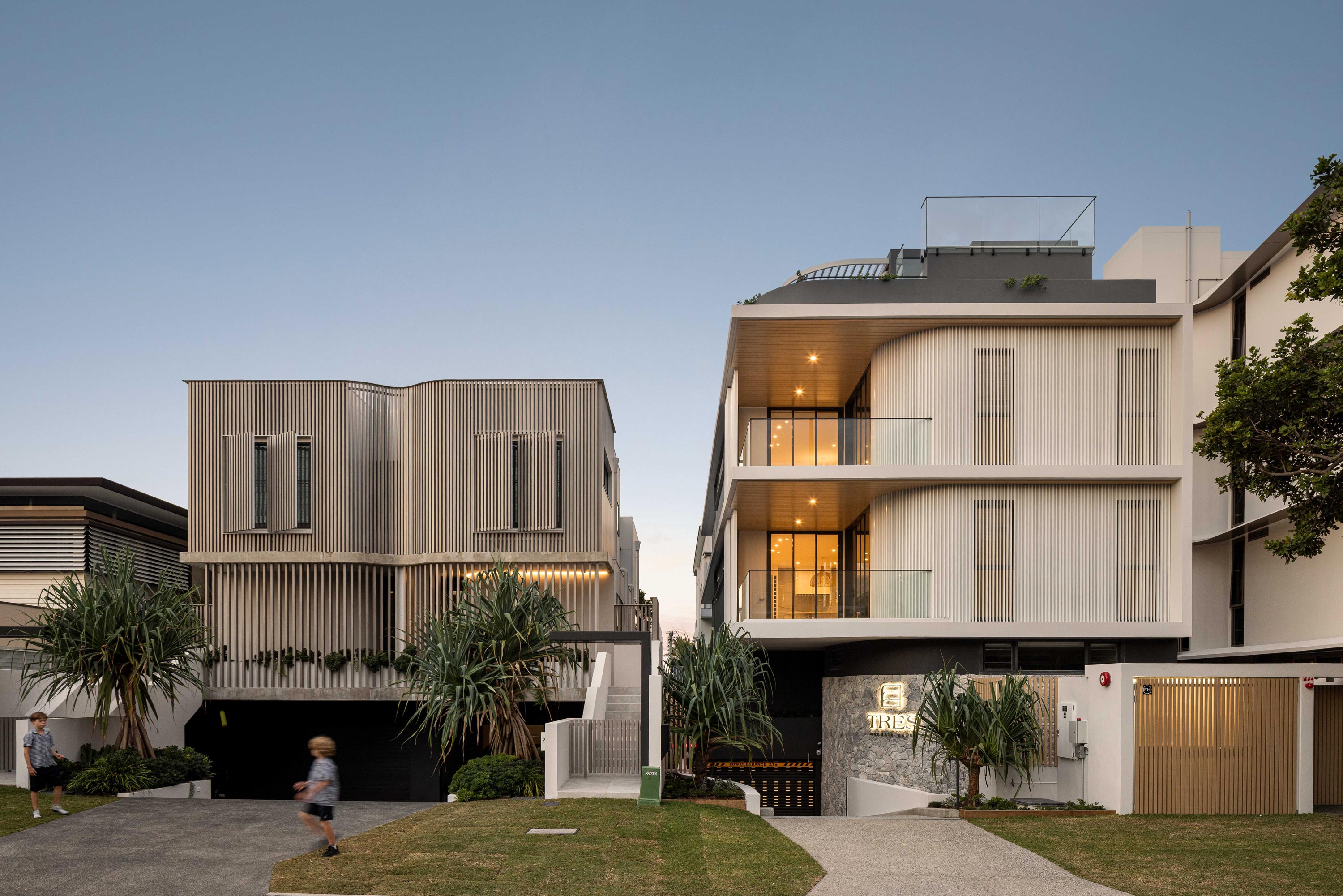 Two modern apartment buildings with balconies and a parked car in front, showcasing contemporary architecture and design.
