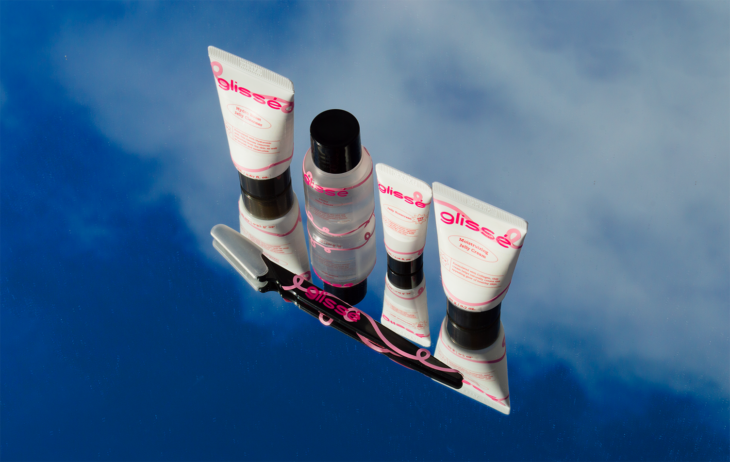 Outdoor mirror photography shot featuring a bright vivd blue sky and white puffy clouds as the background. It features all 5 skin care products that glisse offers.