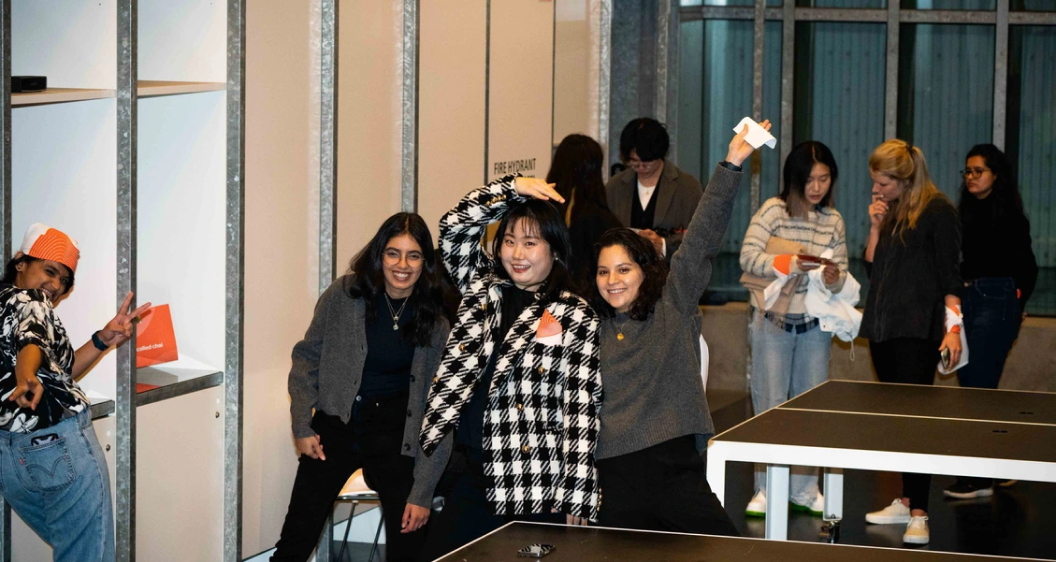 Four femme presenting students, in an exhibition hall, smiling at the camera.