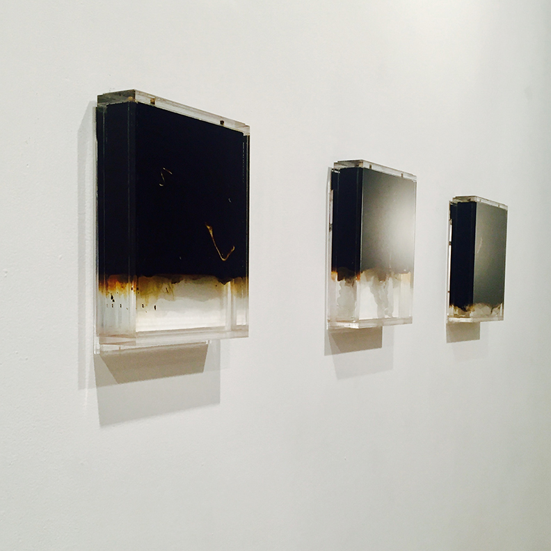 2/4 — OIL AND WATER  6/2 (48 oz. Texas Crude Oil, 16 oz. Illinois Tap Water, remnants of single-use plastic shopping bag).5/3 (40 oz. Texas Crude Oil, 24 oz. Illinois Tap Water, remnants of single-use plastic shopping bag).7/1 (56 oz. Texas Crude Oil, 1 oz. Illinois Tap Water, remnants of single-use plastic shopping bag).Installation view of the project; crude oil, tap water, single-use plastic shopping bags, custom fabricated liquid-tight acrylic; all individual works are 10 1⁄2" x 8 7⁄8" x 1 1⁄2"; 2016.