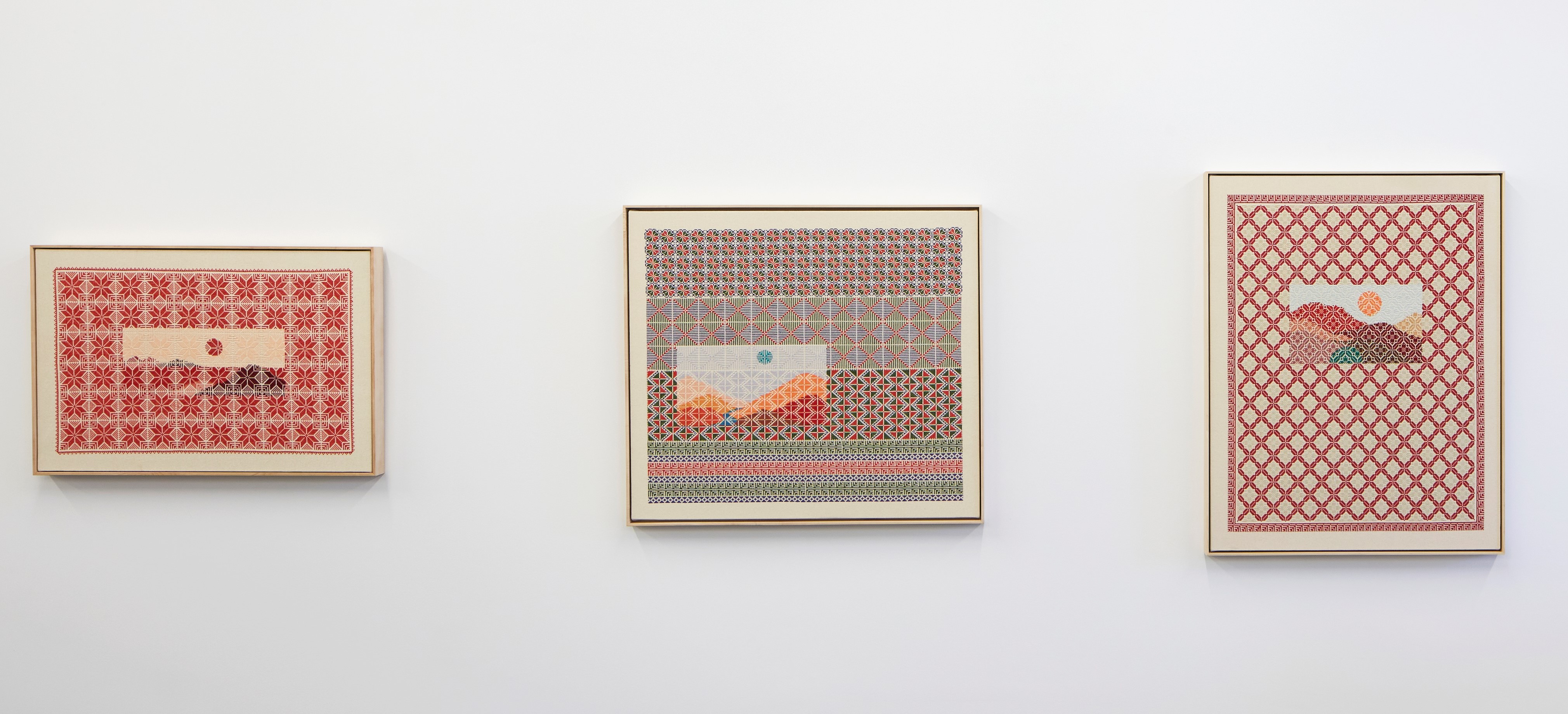 A set of three wall hanging and framed embroidery pieces that feature tight geometric patterns that then have small rectangular natural landscapes superimposed on top in certain sections. The colors are mostly warm: reds, yellows, and browns but also some greens and blues.