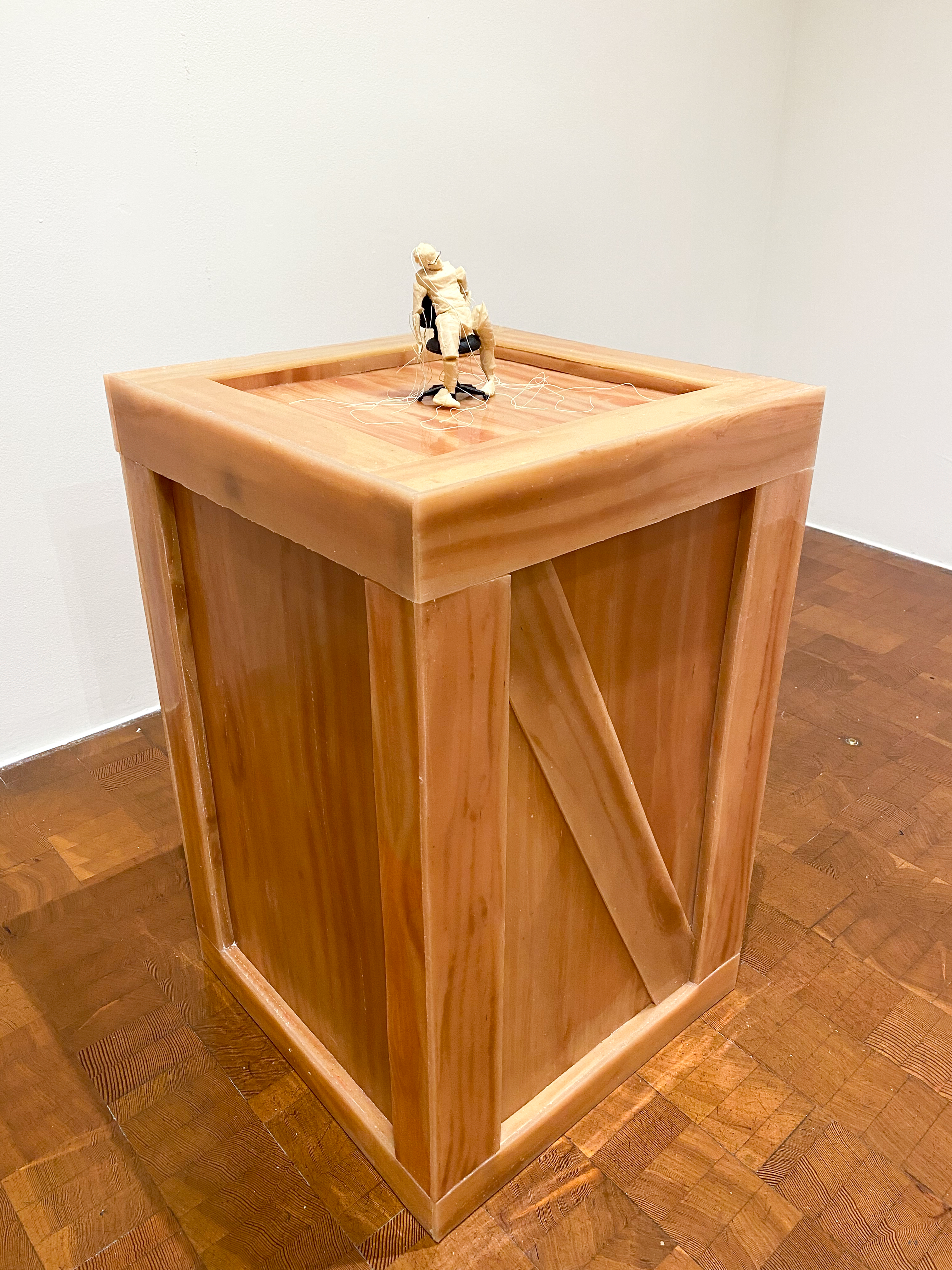 A small 6 or so inch plastic model of the artist, sitting limply in an appropriately scaled swivel chair with marionette strings draping around. All on top of a wooden crate.