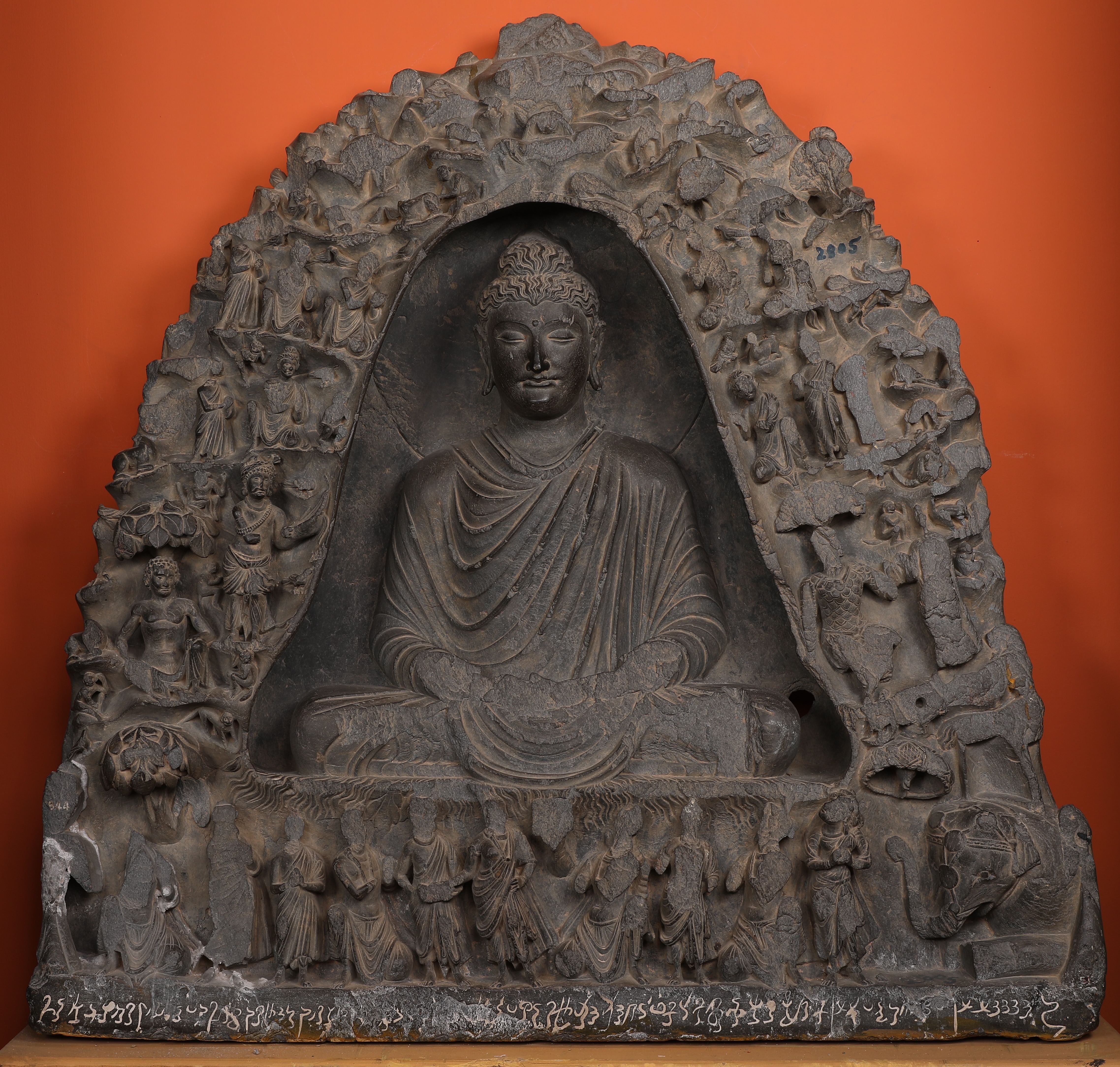 Indrasaila CaveThe sculpture captures a serene moment when the Buddha is deep in meditation within a cave. The god Indra, seeking the Buddha's wisdom, enlists the aid of a harpist (Buddha's right) to gently rouse him from his trance.Material: SchistDimension: Height: 76cm; Width: 75.1 cm; Depth: 7 cm