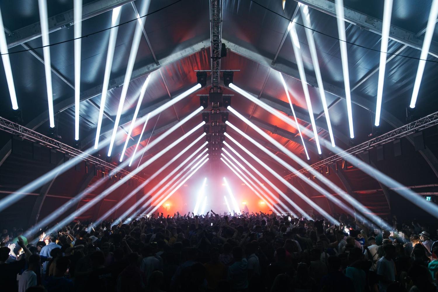 Packed crowd inside AVA Festival Pumphouse with dramatic white beams of stage lighting