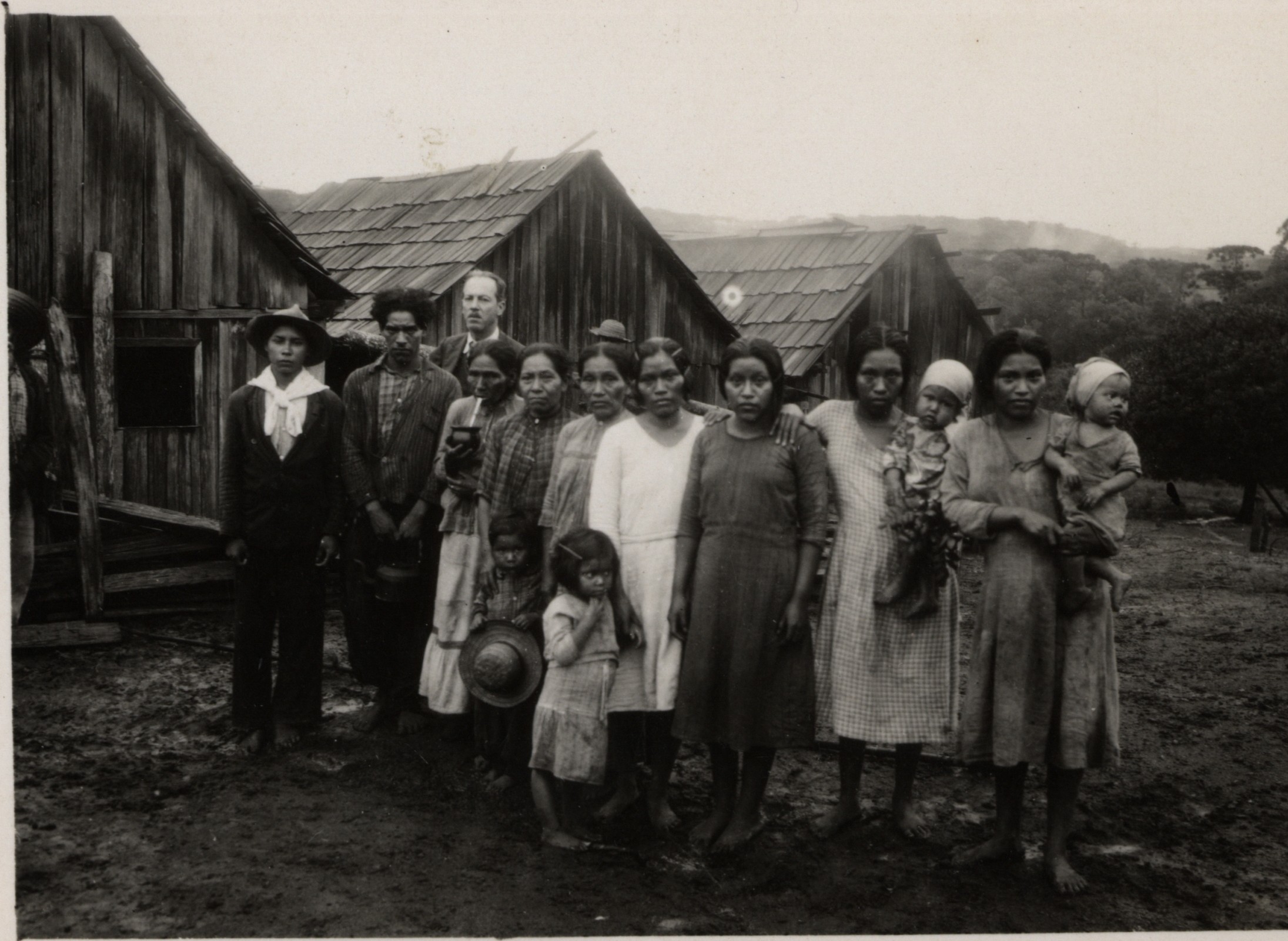 Autoria desconhecida, Grupo de indígenas Kaingang e homem branco em frente a habitações de madeira, s.d.