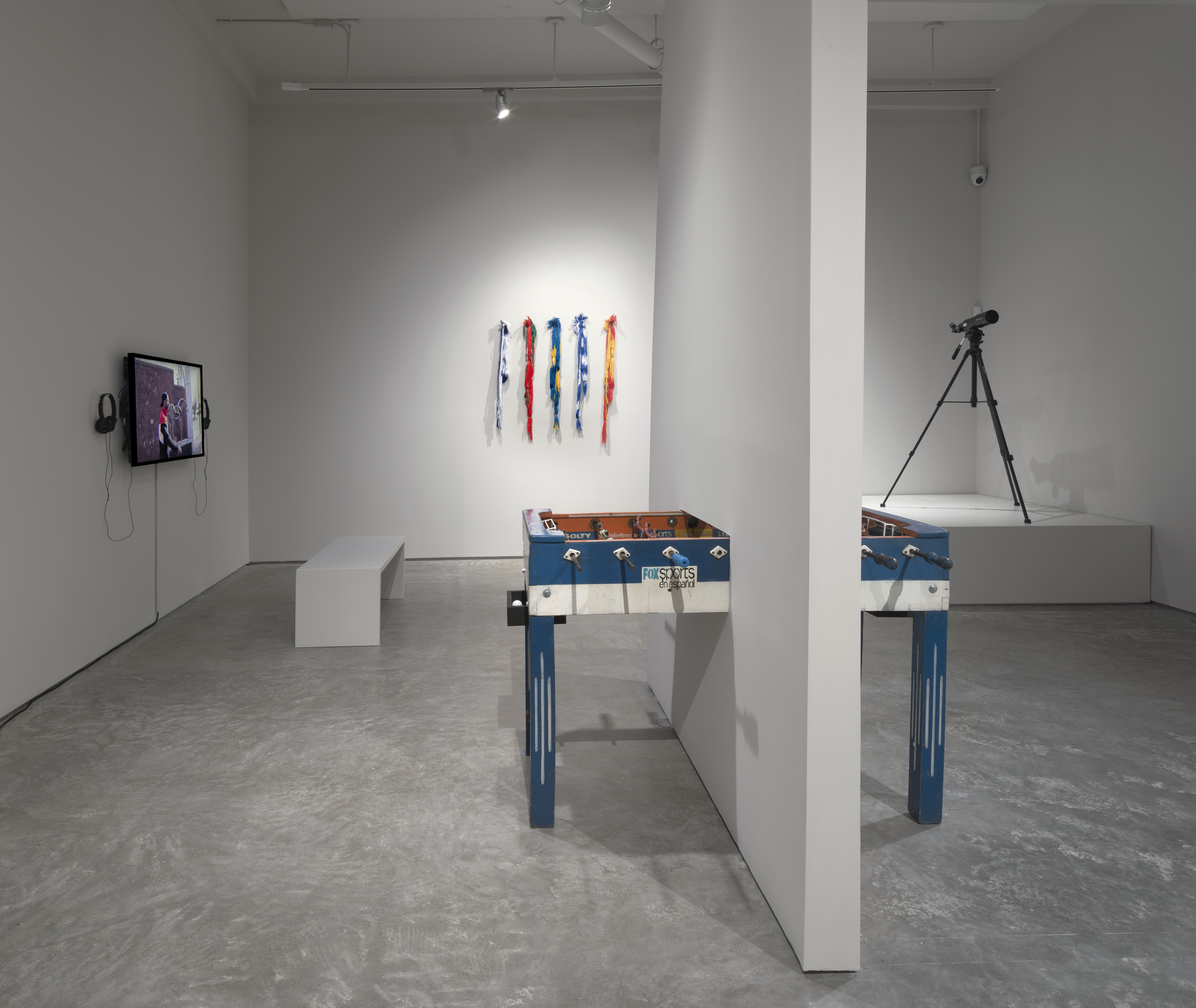 From left to right: Juan Obando, Museum Mixtape, 2014, Video, 22 minutes. Regina Parra, Metegol, 2014, hand painted Bolivian foosball table, 3' x 2'2" x 4'3." Sanne Vaassen, from the series FLAGS, 2016, Unravelled flags, left to right: Israel, Portugal, Sweden, Greece, Spain, dimensions variable. Rainier Leyva Novo, Eternamente te Esperaré, 2015, video, telescope, 10:06 minutes.