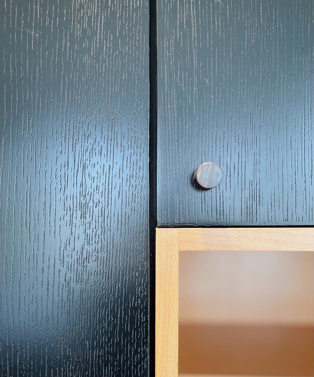 Close-up detail photo of the Brant Beach renovation's dark textured kitchen cabinetry with a simple round pull, next to a light wood open shelf.