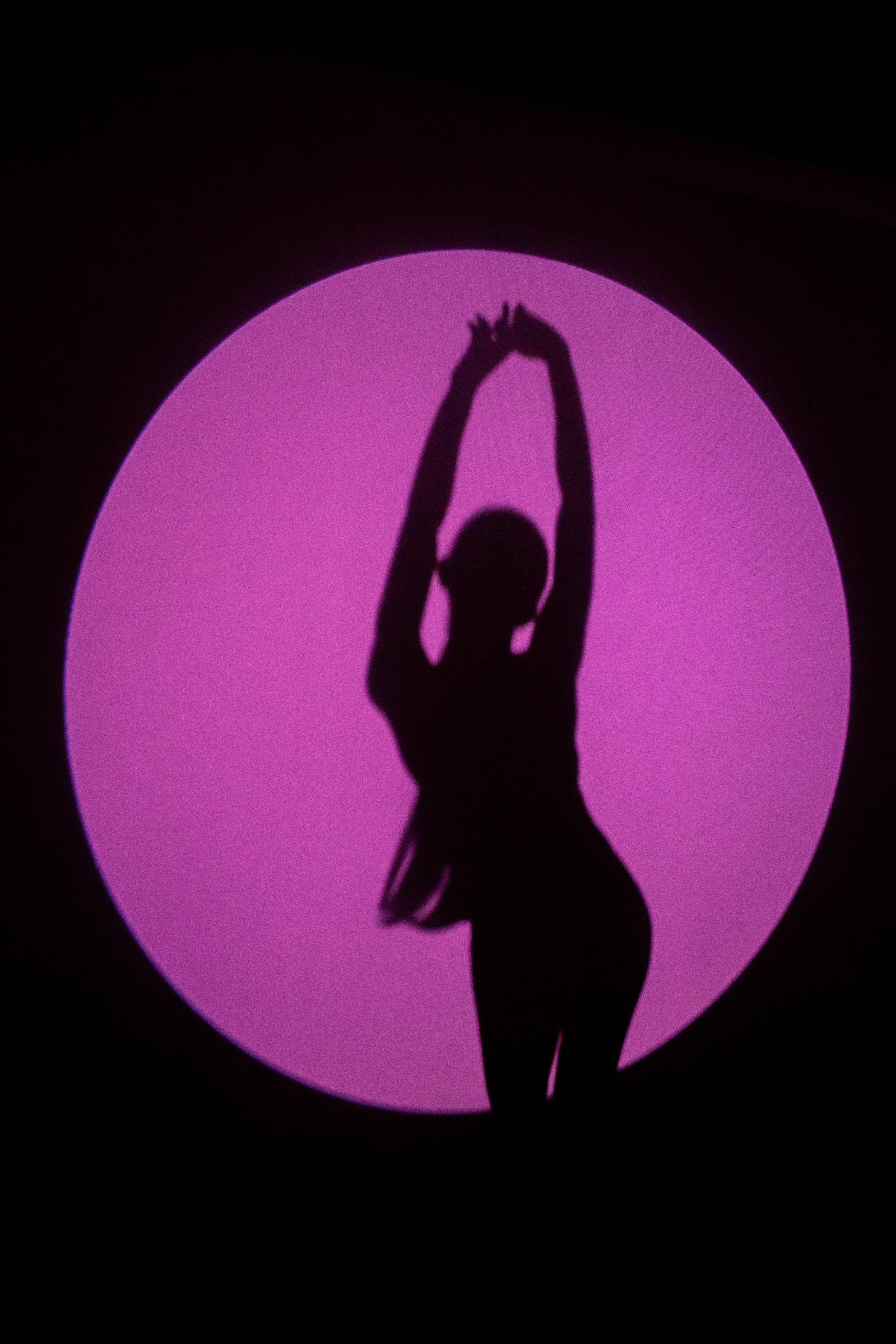 Striking silhouette of a woman, Emilia Kaplan, framed within a bold pink circle, emphasizing her figure through light and shadow. A minimalist yet high-impact fashion composition.