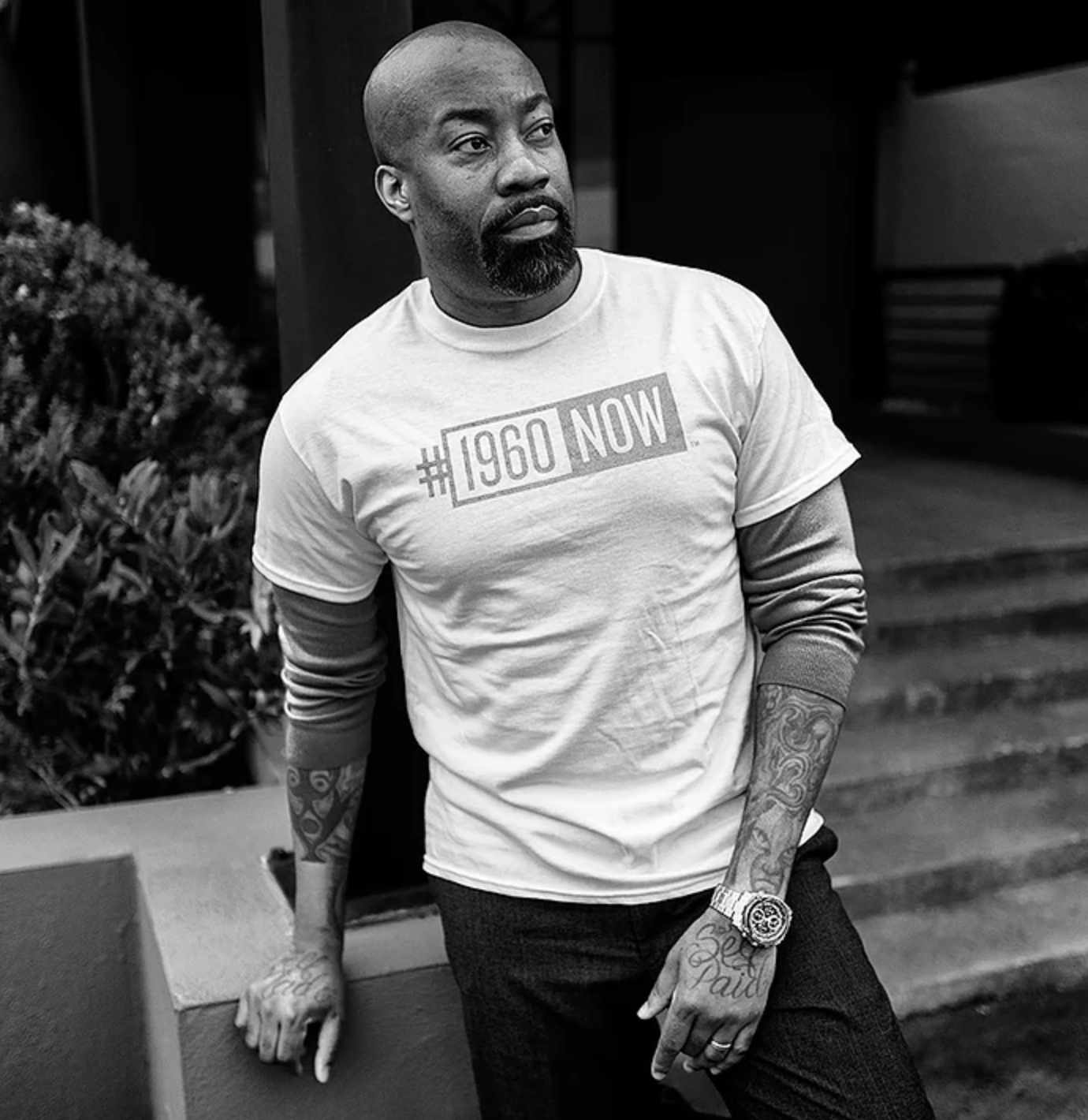 Black and white image of man wearing a white shirt displaying the #1960Now logo.