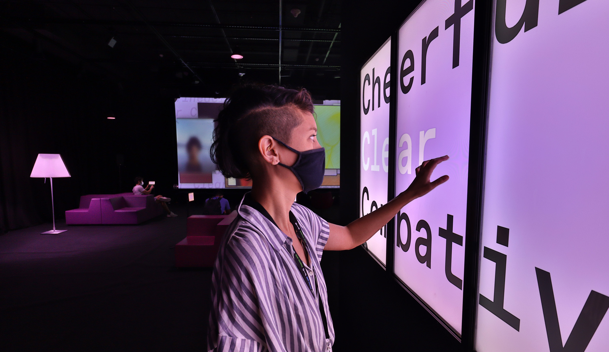 artist touches a bank of four vertical toucscreens, selecting the emotion clear, screens and people in the background