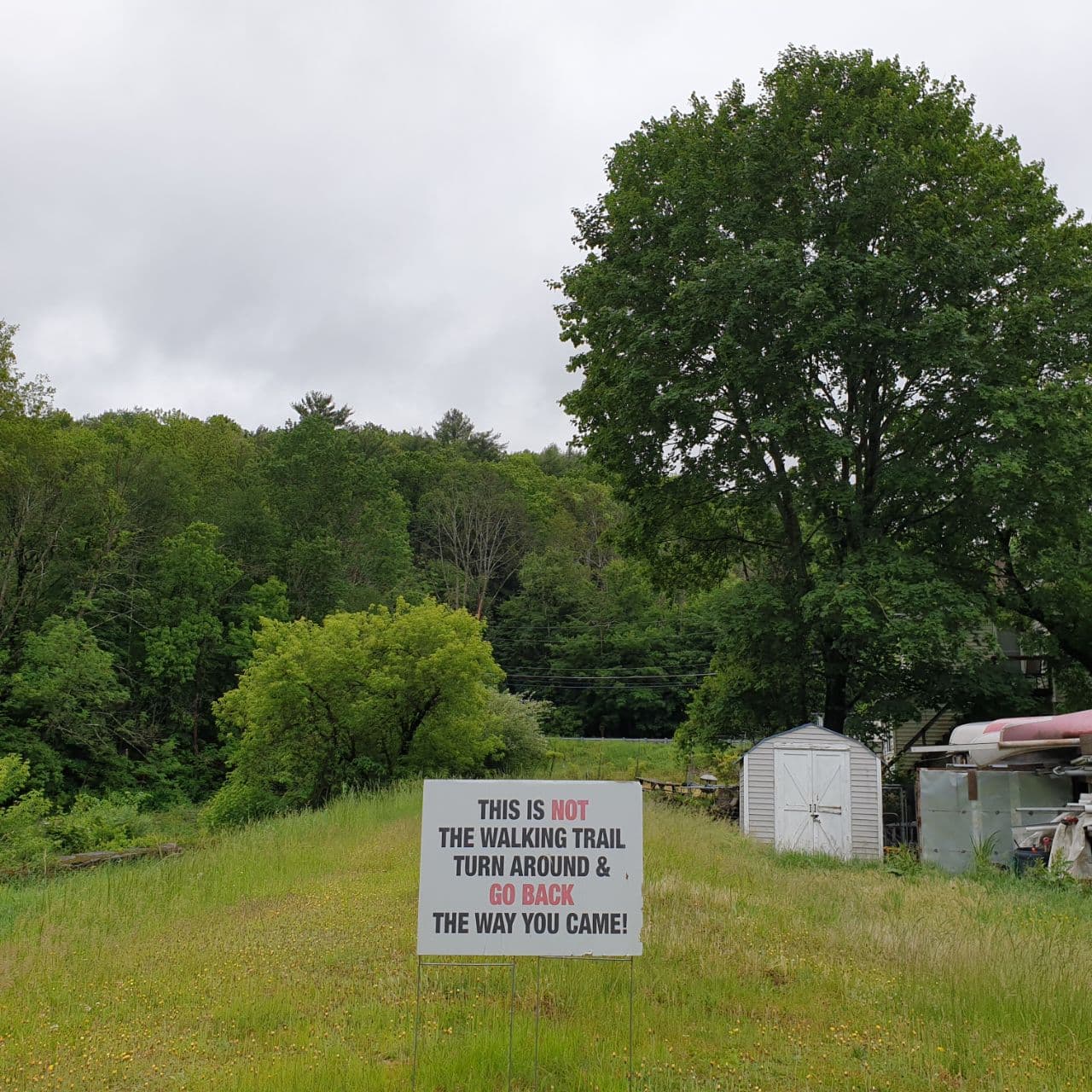 A sign on a grass path that says "This is not the walking trail, turn around and go back the way you came!"
