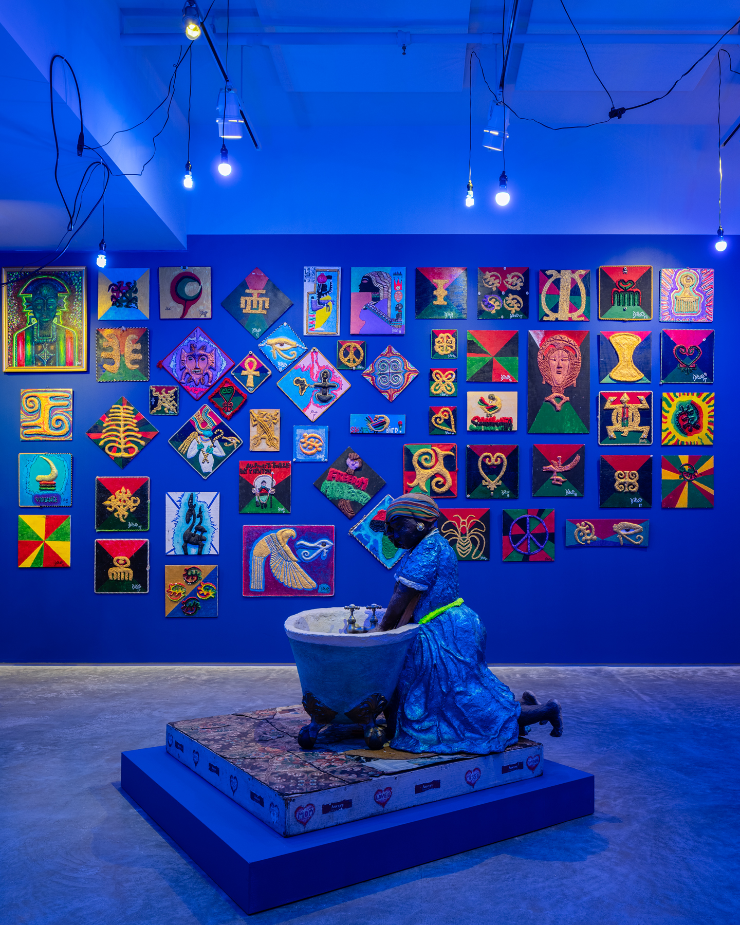 Washerwoman, 1996, Papier-mâché, fabric, jewelry, linoleum floor tile, antique washboard. Wall of Adinkra symbols. 