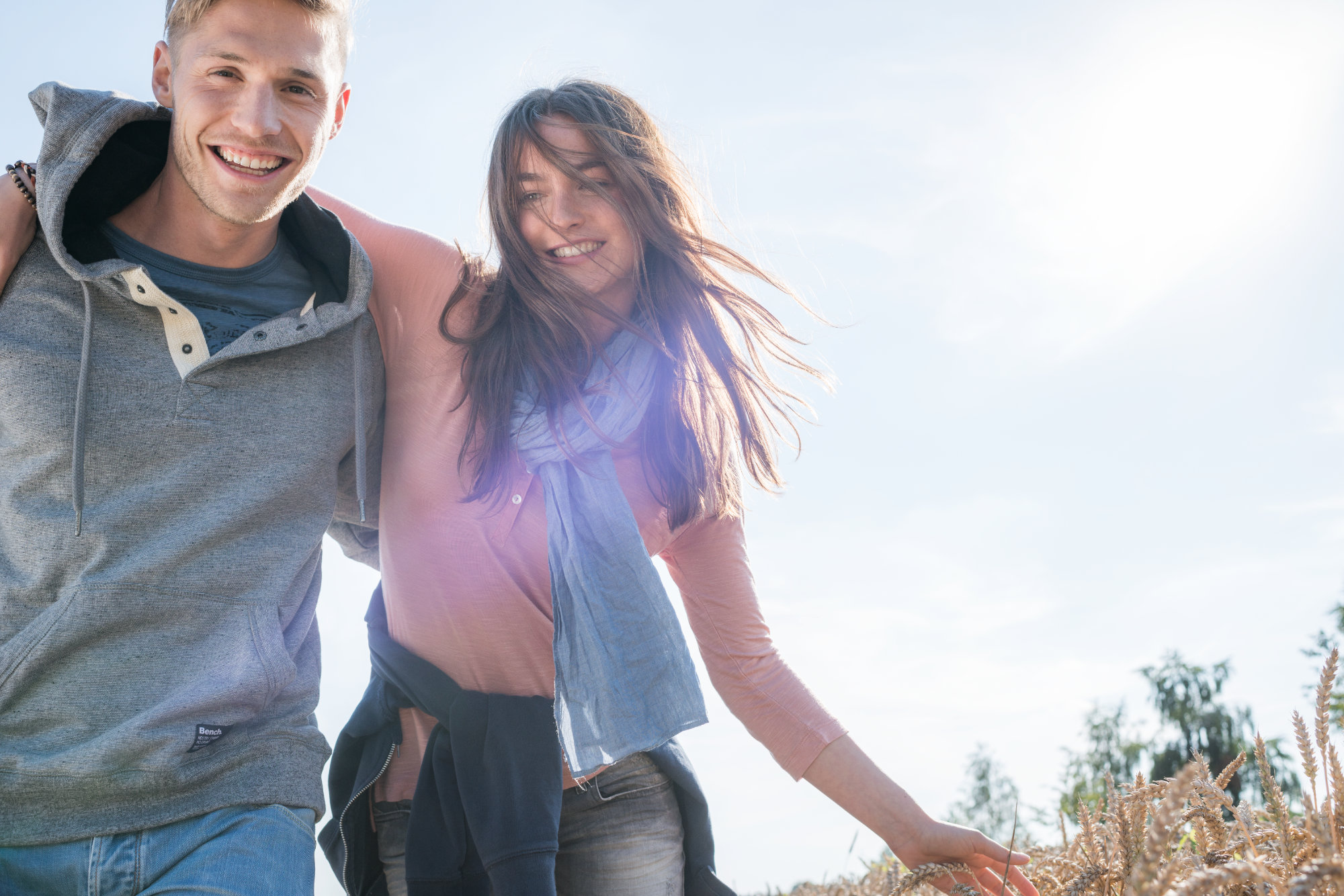 Ein junges Pärchen geht Arm in Arm an einem Kornfeld entlang.