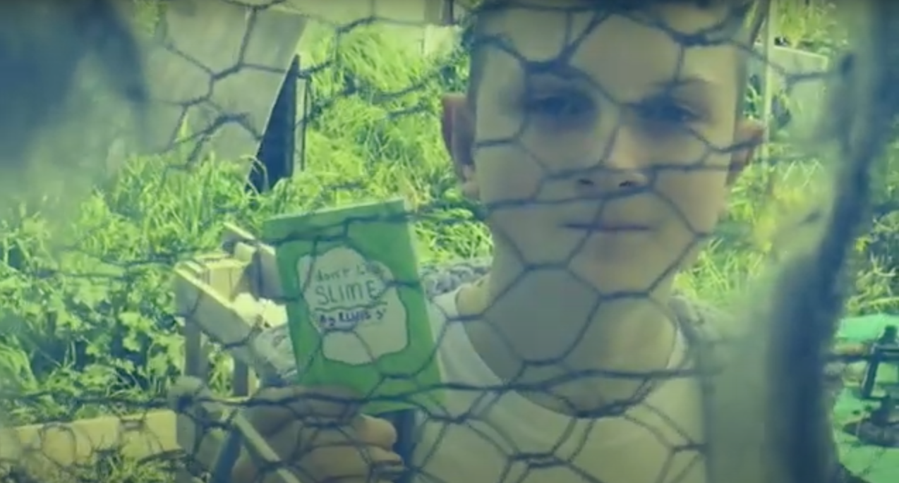 zinemaker Elvis Sorocuk obscured by wire mesh, holding his zine "i don't like slime"