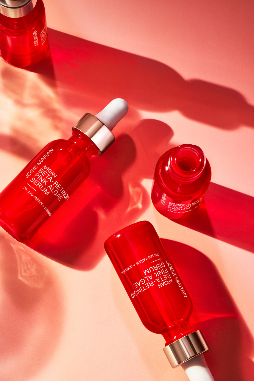KMA stylist Sara Wacksman designs set for photo of many shiny red bottles of serum on a pink background for Josie Maran