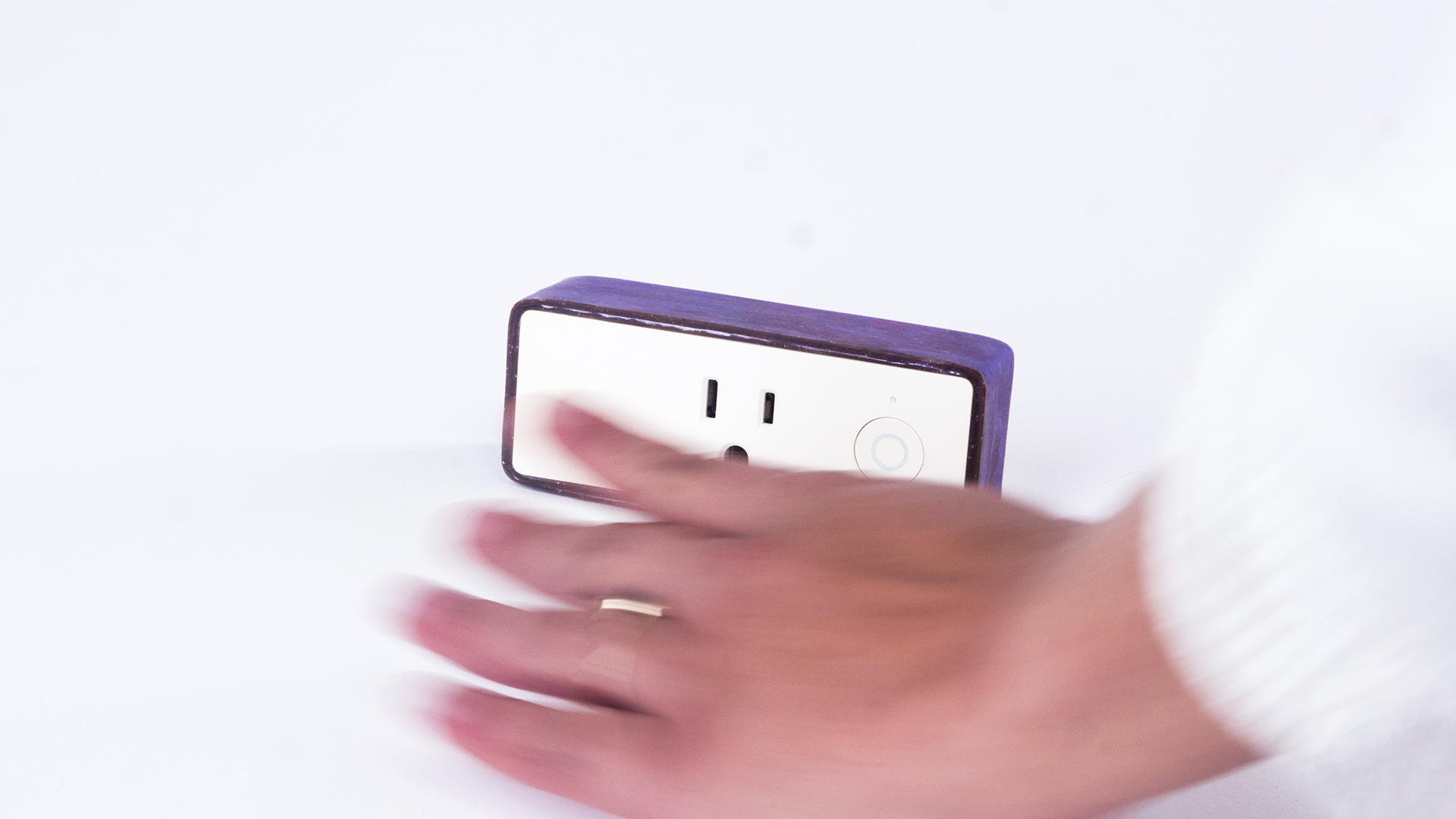 a rectangular outlet with purple edges and a white surface where the outlet is and a blurred hand in front of this device.