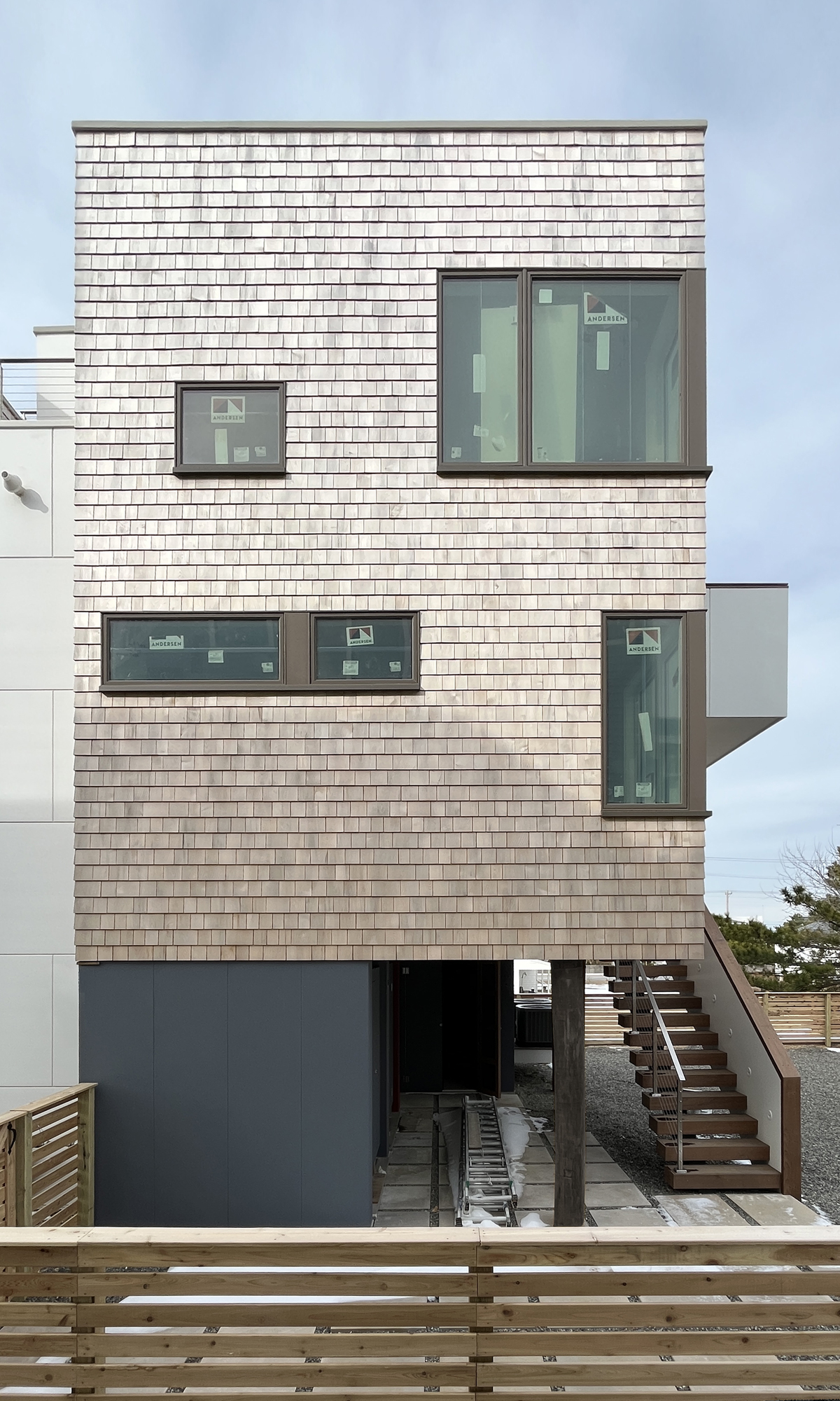 Construction photo of The Gap House at the finish line, showing the completed natural cedar shingle facade, modern windows, and exposed metal staircase in soft winter light.