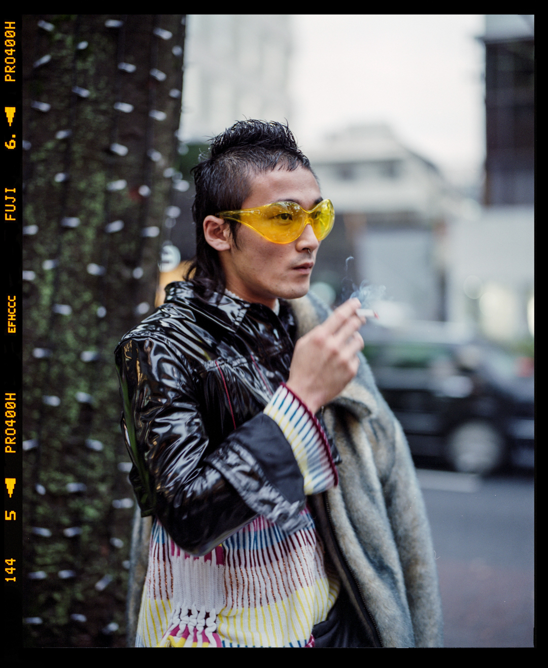 A young Japanese stylist with yellow-tinted glasses and PVC jacket in Omotesando