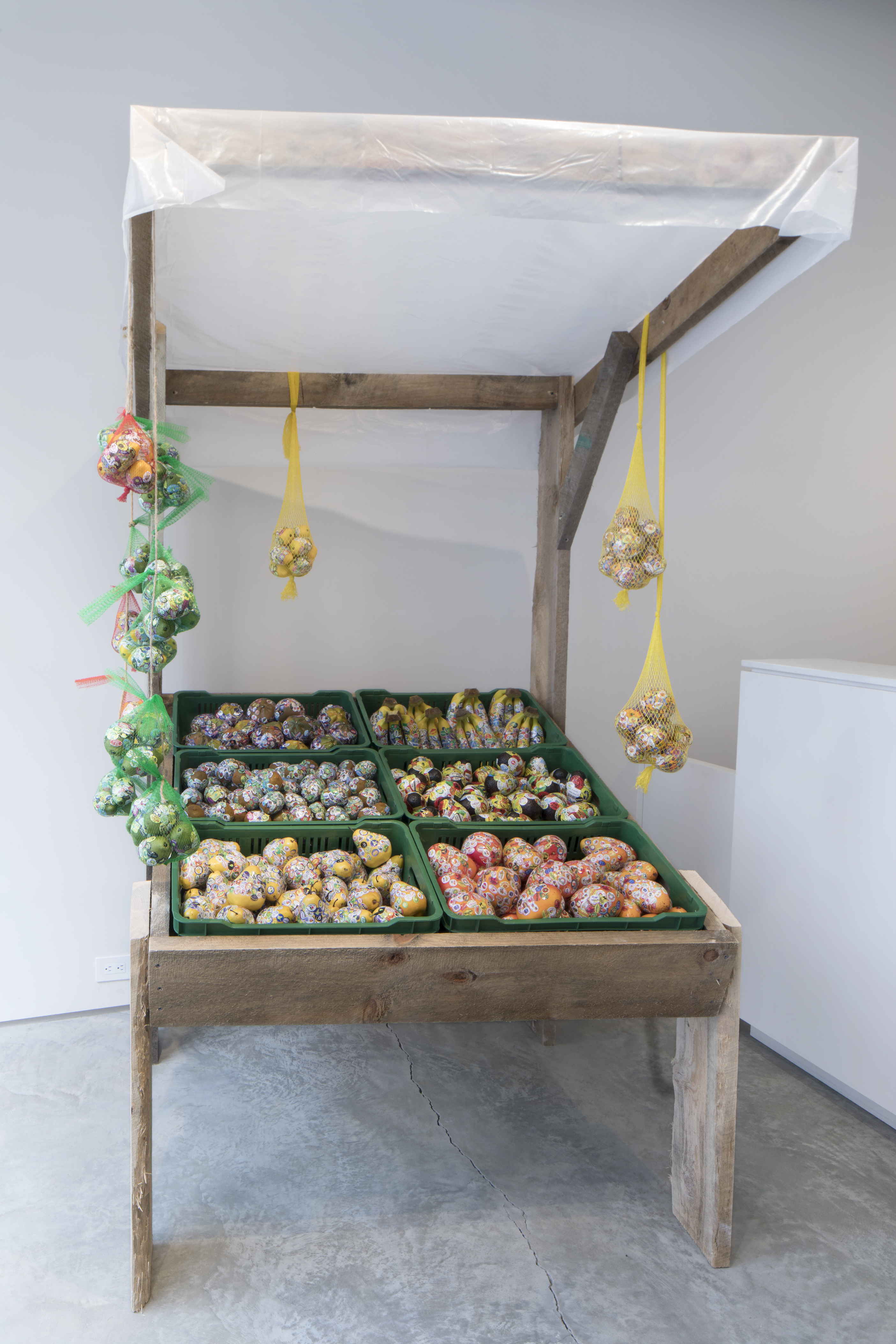 Adriana Martinez, Tutti Frutti Market, 2018, plastic fruits, stickers, six plastic crates, wood, mesh, 7' x 4' x 4.'