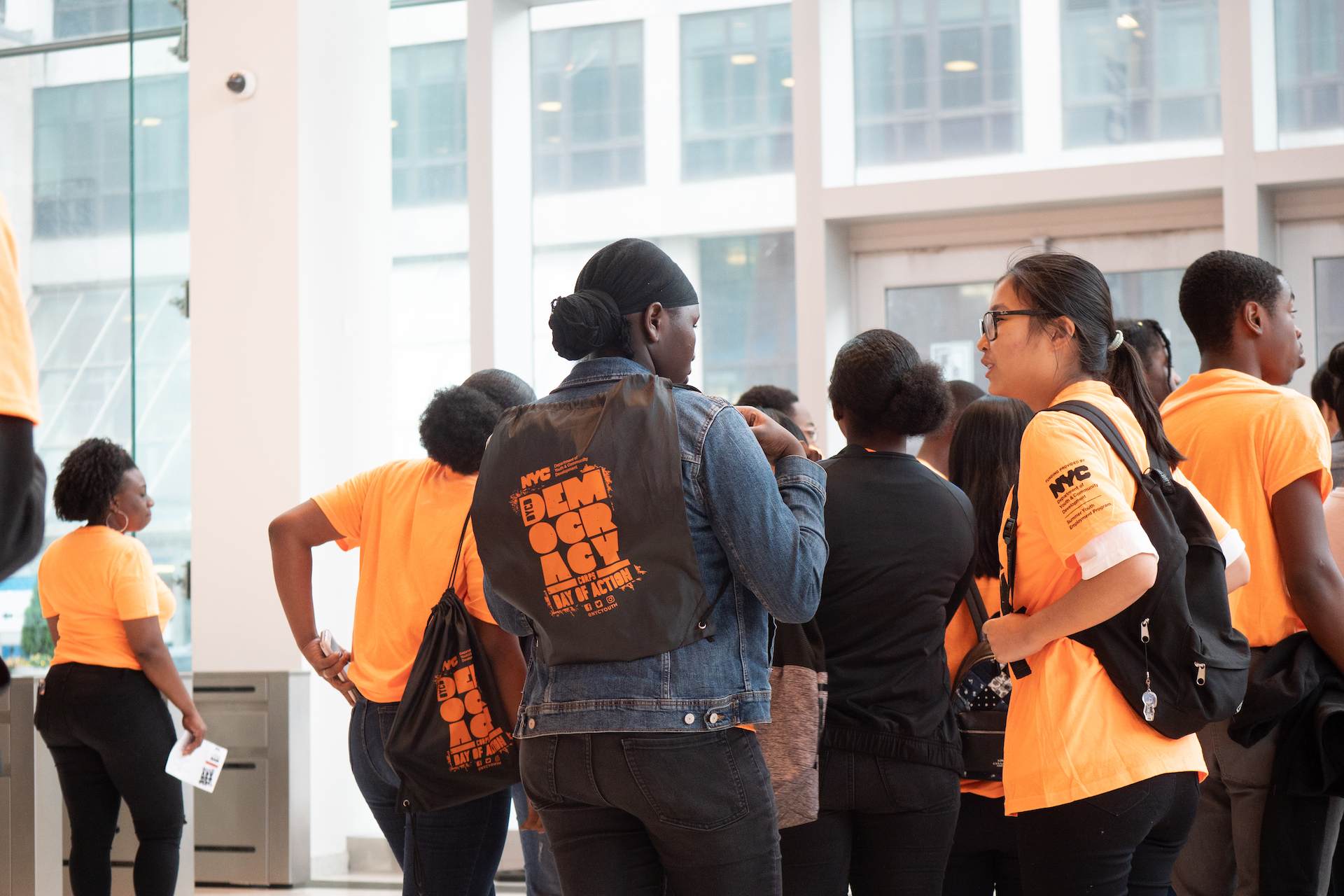 A group of youth participants socializing while wearing black and orange branded Democracy Corps apparel.