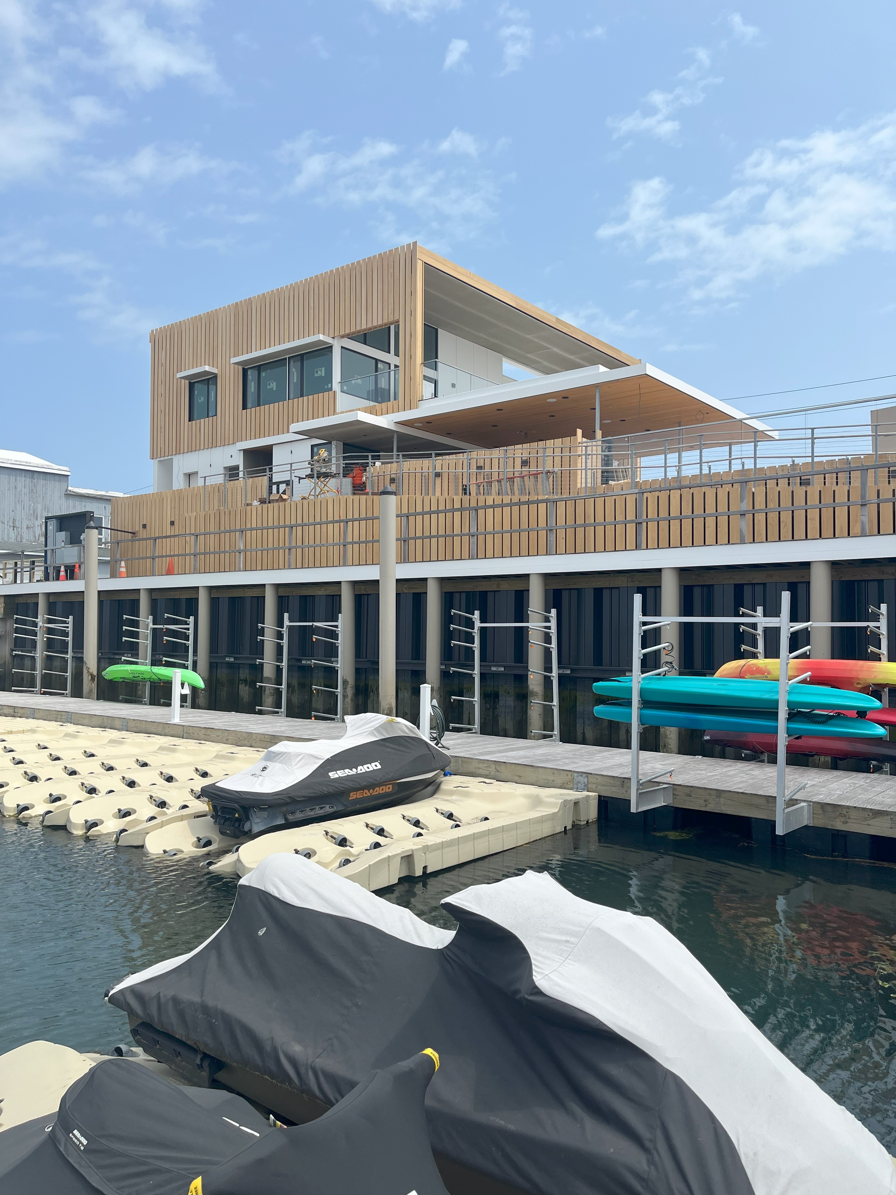 Exterior view of the Brigantine Marina Paddle Club from the water, showcasing the modern building, docks with jet skis, and kayak storage.