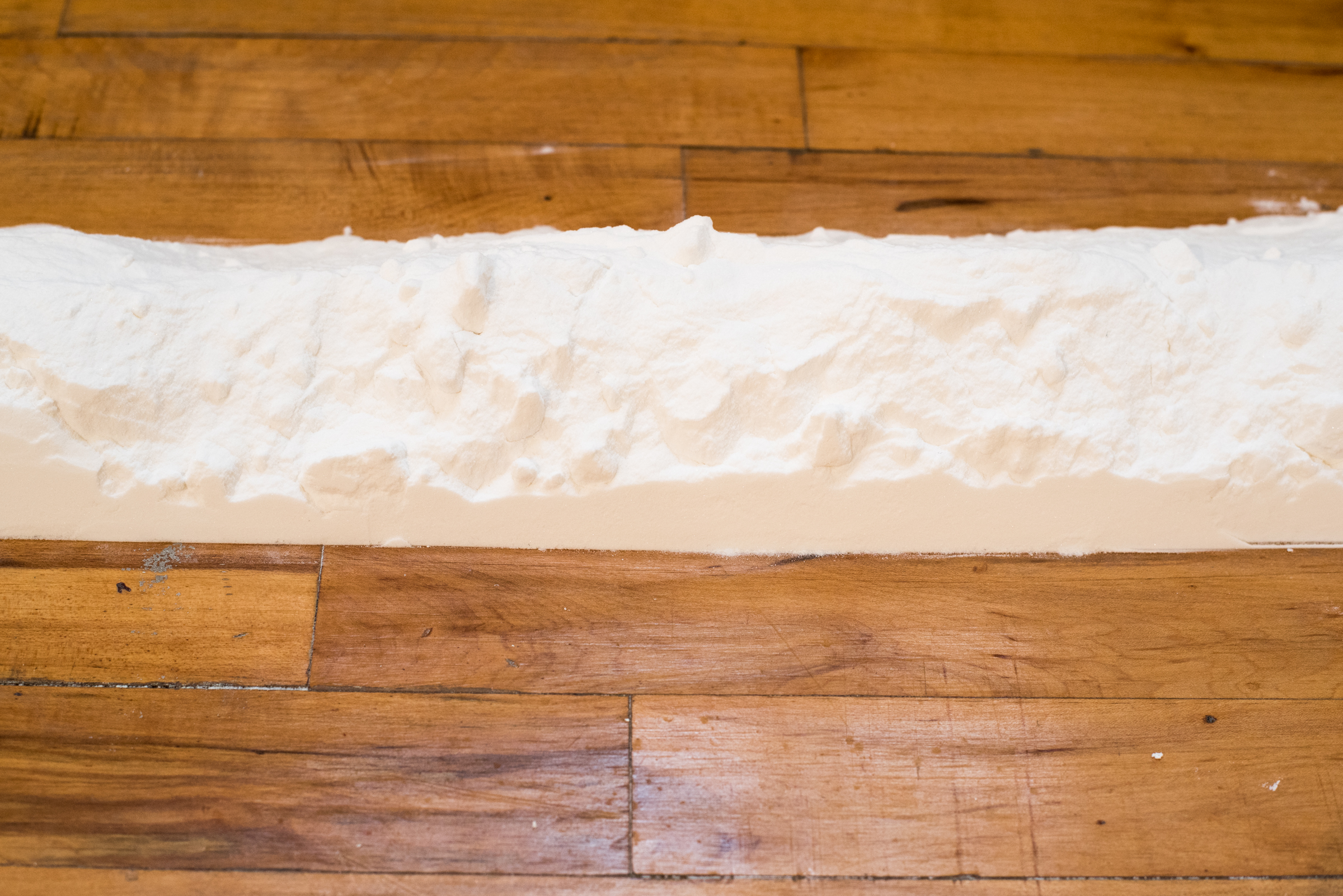 2/3 — A WALL OF FLOUR.  The site-responsive installation A Wall of Flour. 6.12.15 was created for the exhibition Body Mass Index, curated by George William Price.  150 lbs. sodium bicarbonate, floor, dimensions variable, approximately 6" x 540", the distance between work and wall/windows equal to reach of the artist's/activator's arms, 2015.