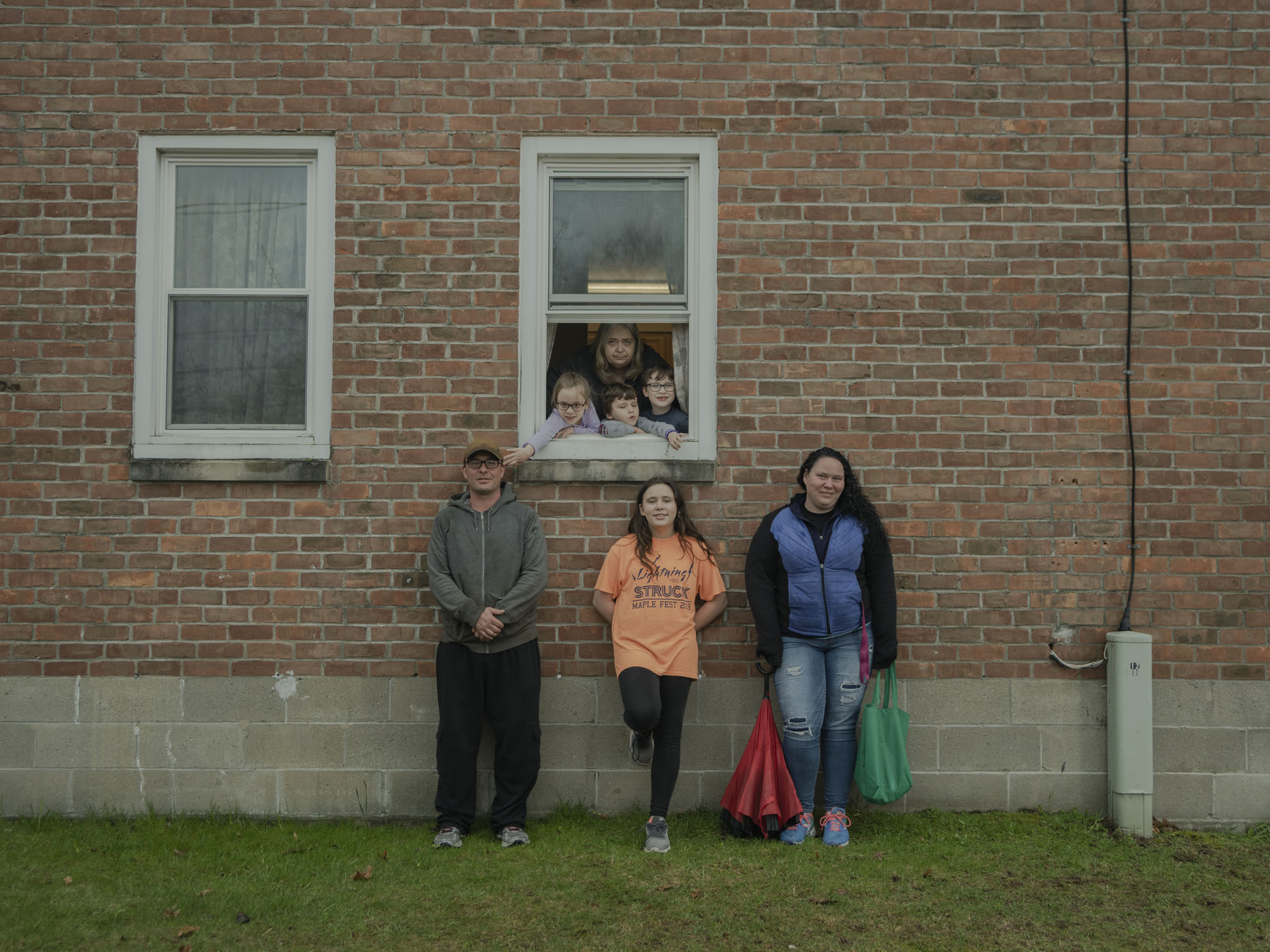 Helen Winchip, in the window, is the main caretaker of her five grandchildren, ages 5 to 16. On visits, her daughter Christine, right, and Christine’s partner, Gary Green, left, talk to their children through the window.